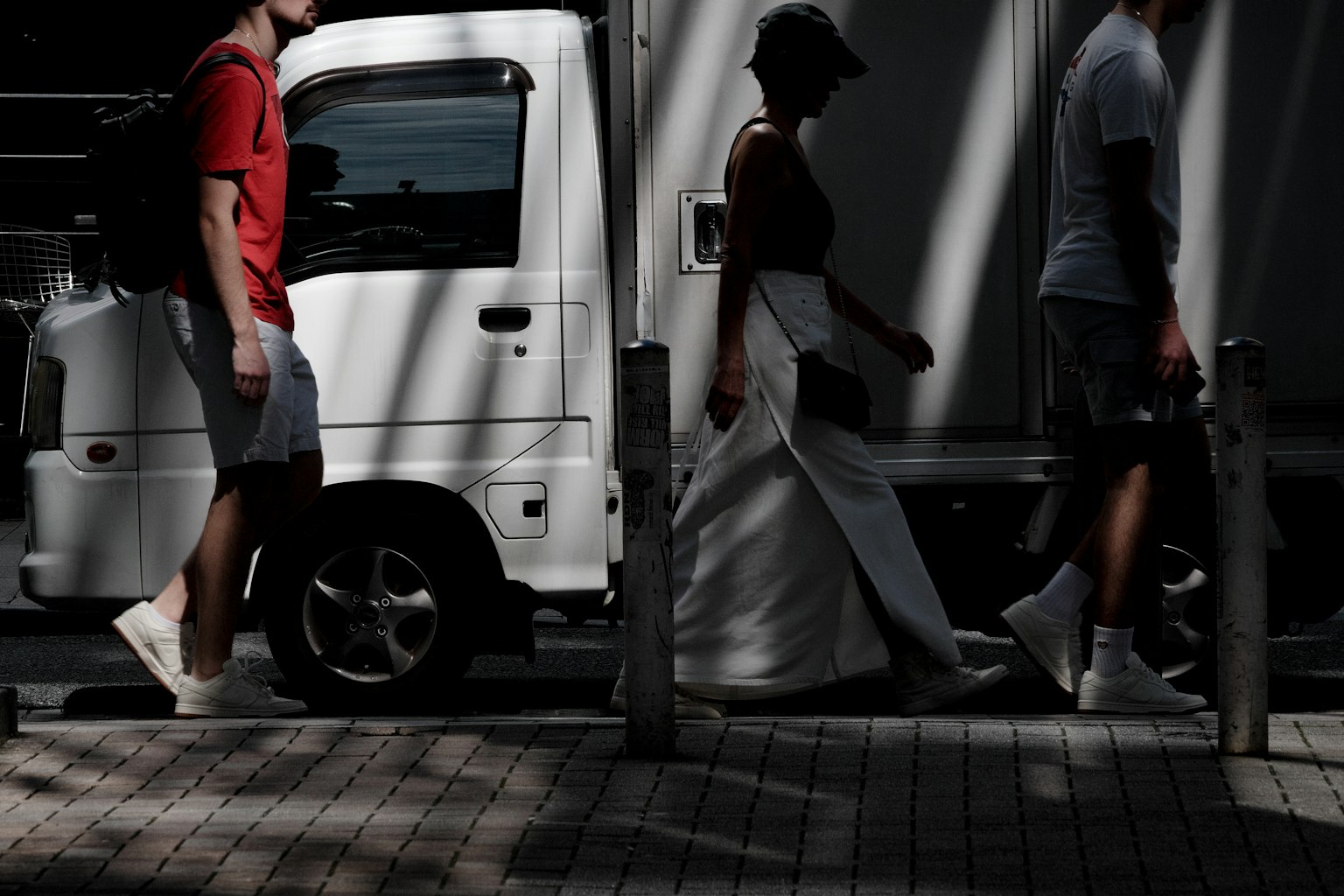 Persone che camminano nell'ombra accanto a un piccolo furgone bianco