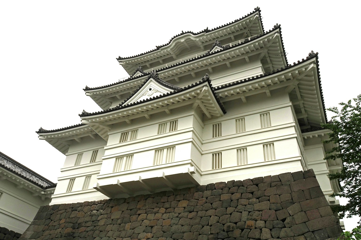 Japanisches Schlossgebäude mit weißer Fassade gestaffelten Dächern und Steinfundament