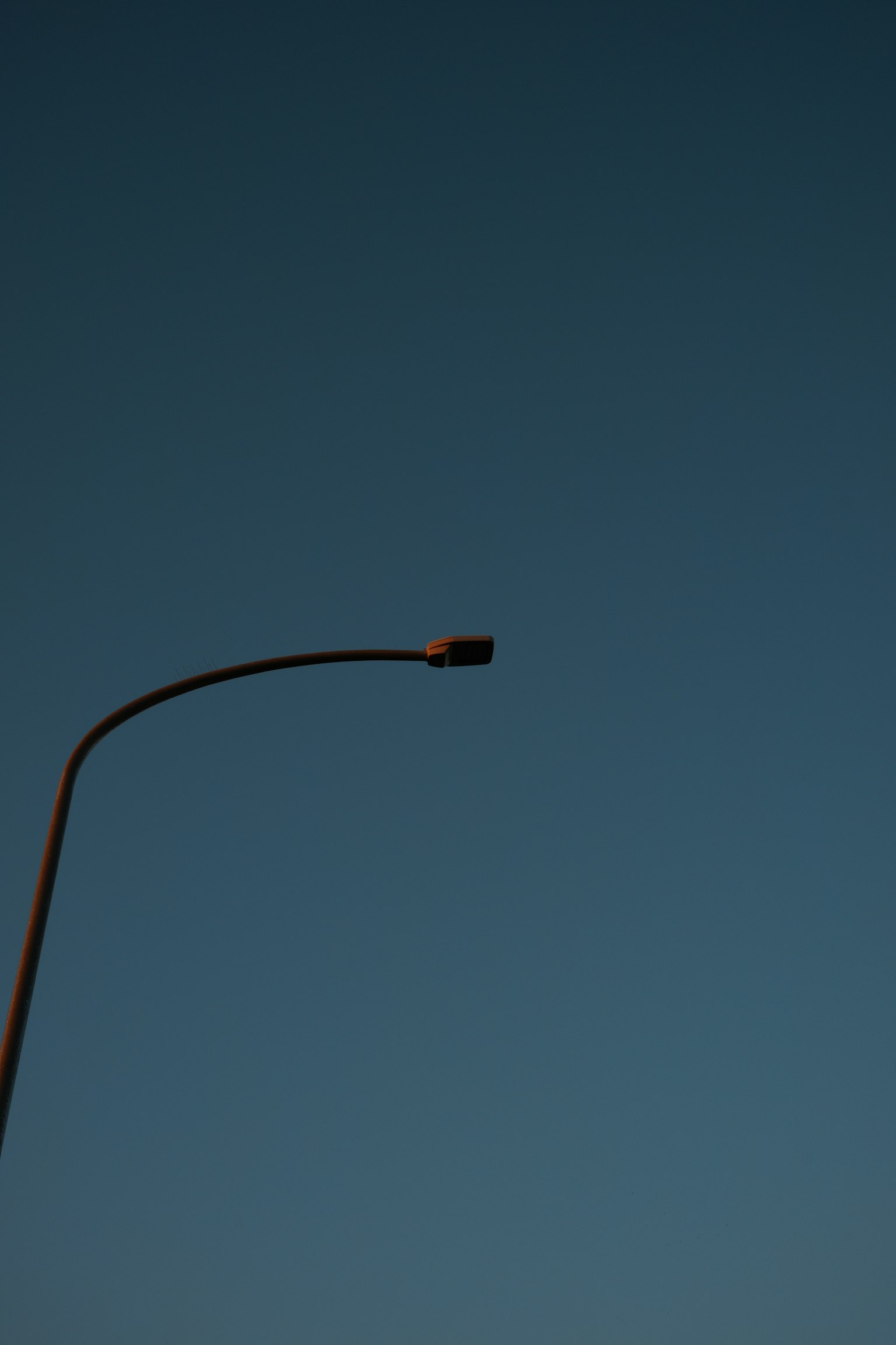 Silhouette of a streetlight against a blue sky