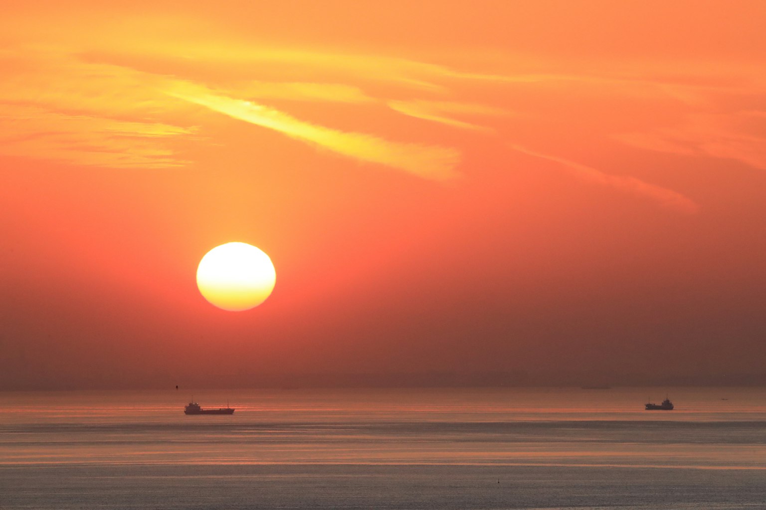 海上橙色日落的场景，两个船只可见