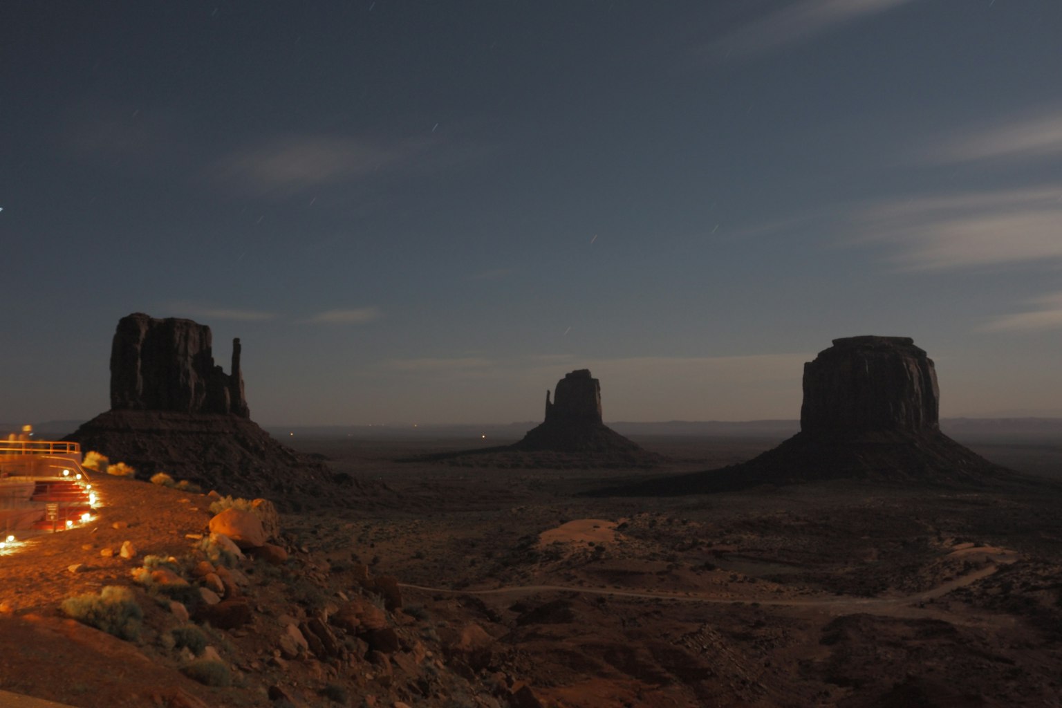 Vista notturna di Monument Valley con tre formazioni rocciose illuminate dalla luce della luna