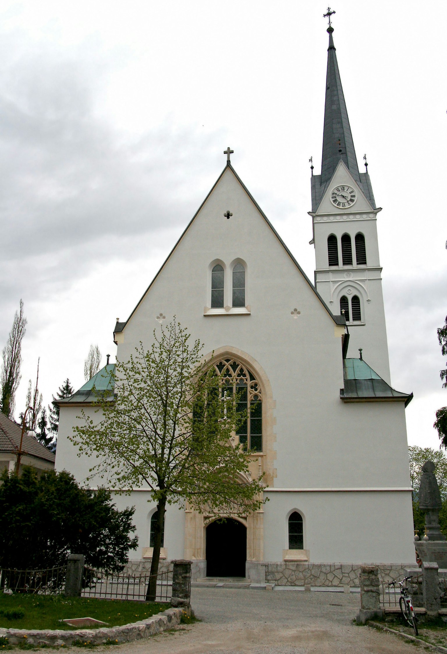 Äußere einer weißen Kirche mit einem Turm umgeben von grünen Bäumen und einem bewölkten Himmel