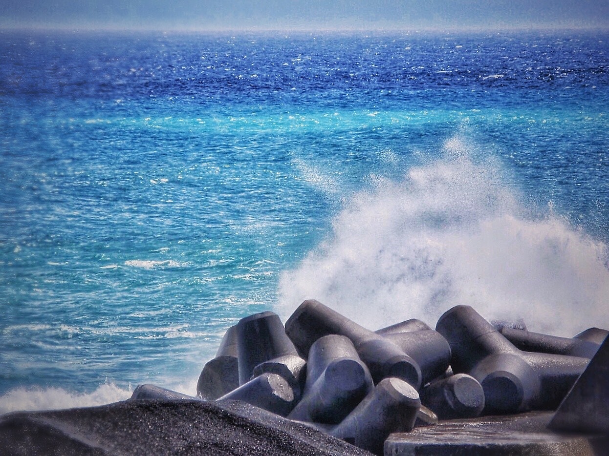 波飛沫が上がる海岸線の青い海と波除ブロック