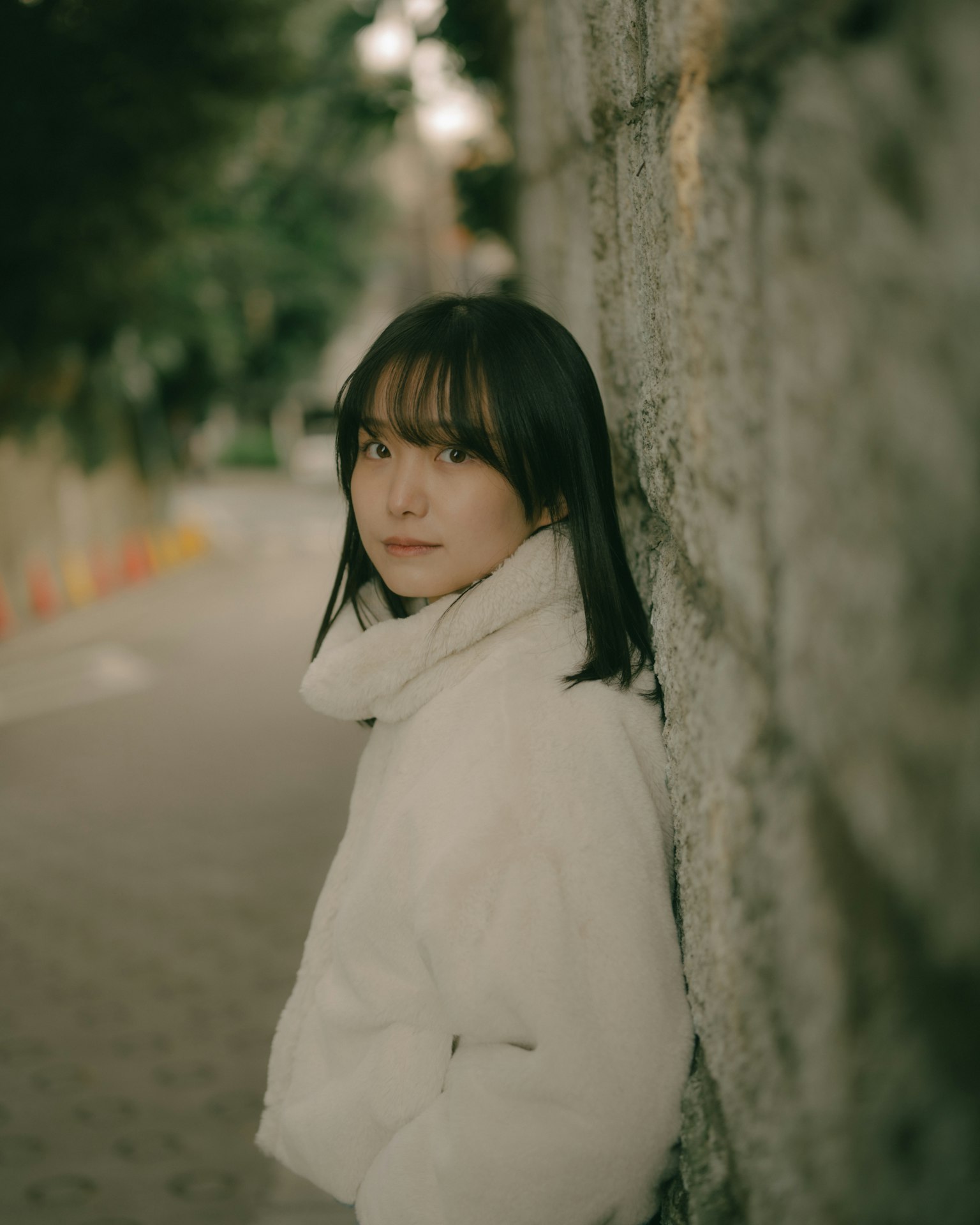 一位穿著白色外套的女性靠在石牆上