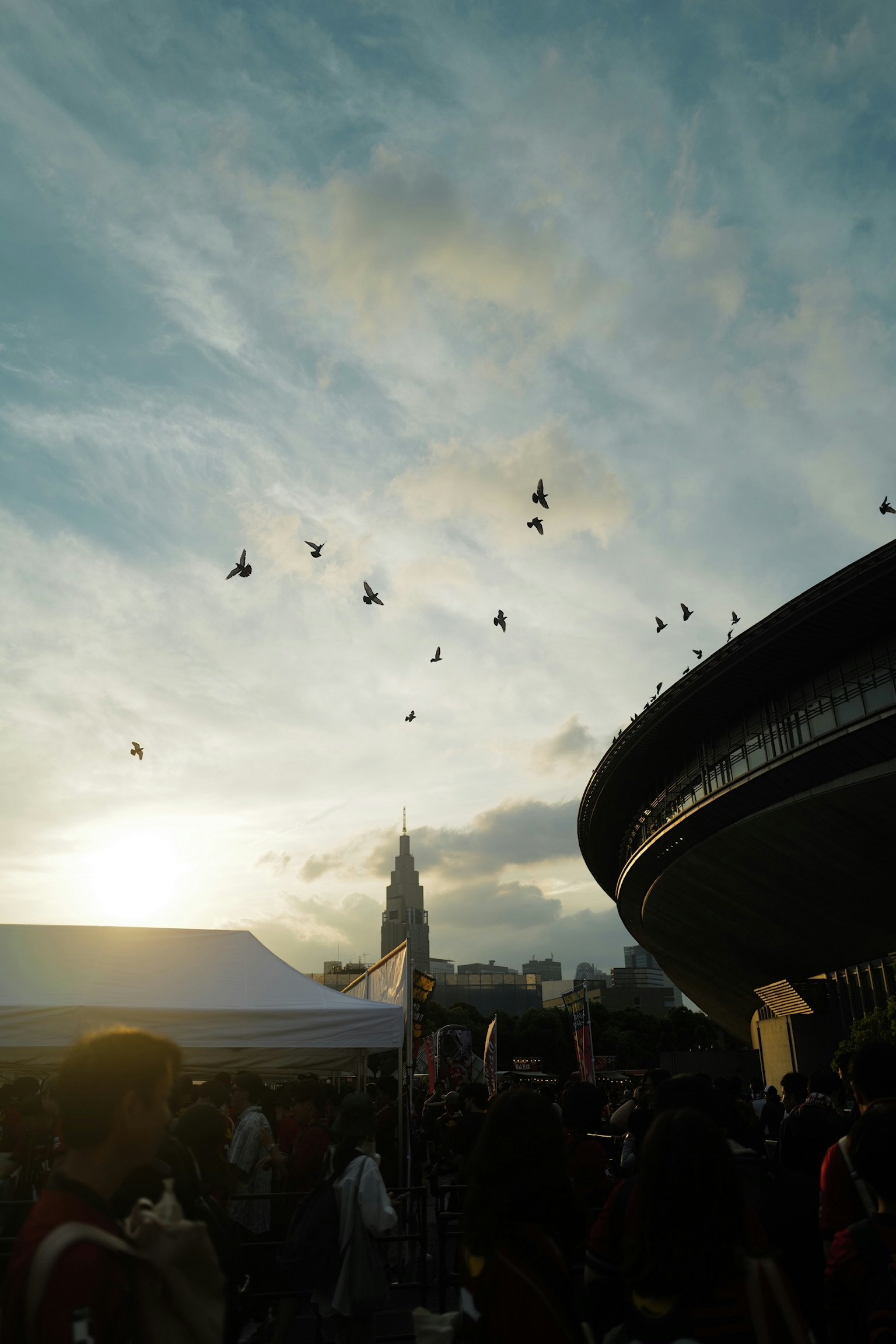 Outdoor event crowd area with birds flying in the dusk sky