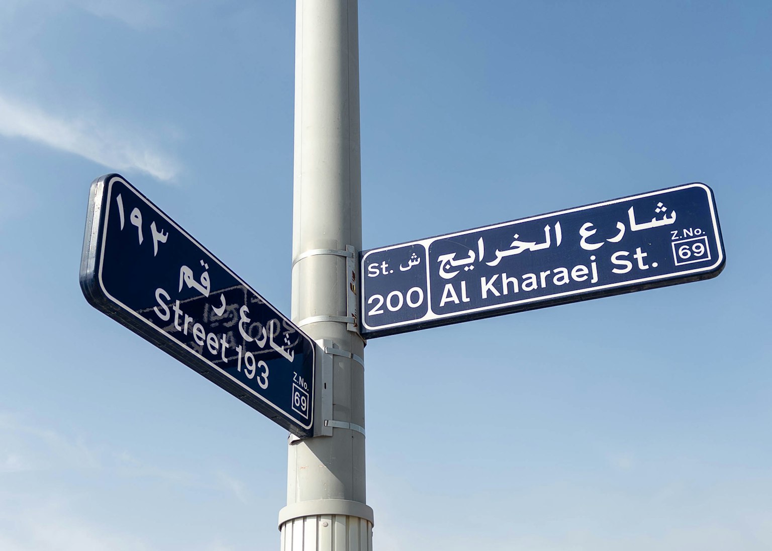 Señal de calle azul que muestra Al Kharaej St 200 en árabe e inglés