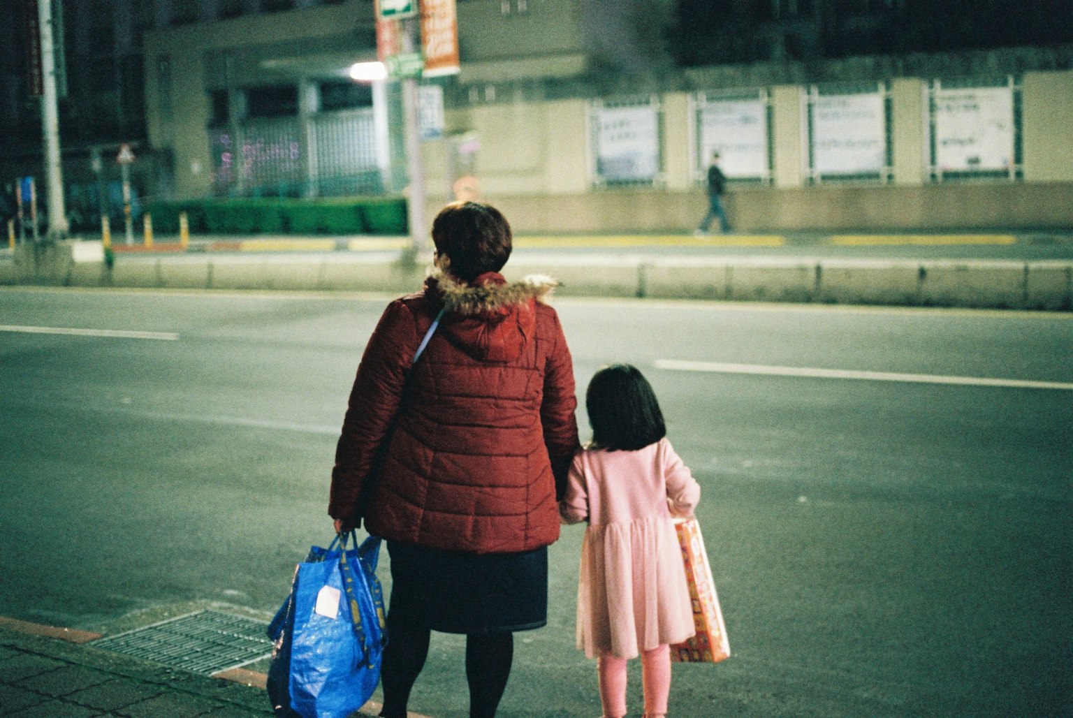 Una donna con un cappotto rosso che tiene per mano un bambino in un vestito rosa in una strada di città di notte