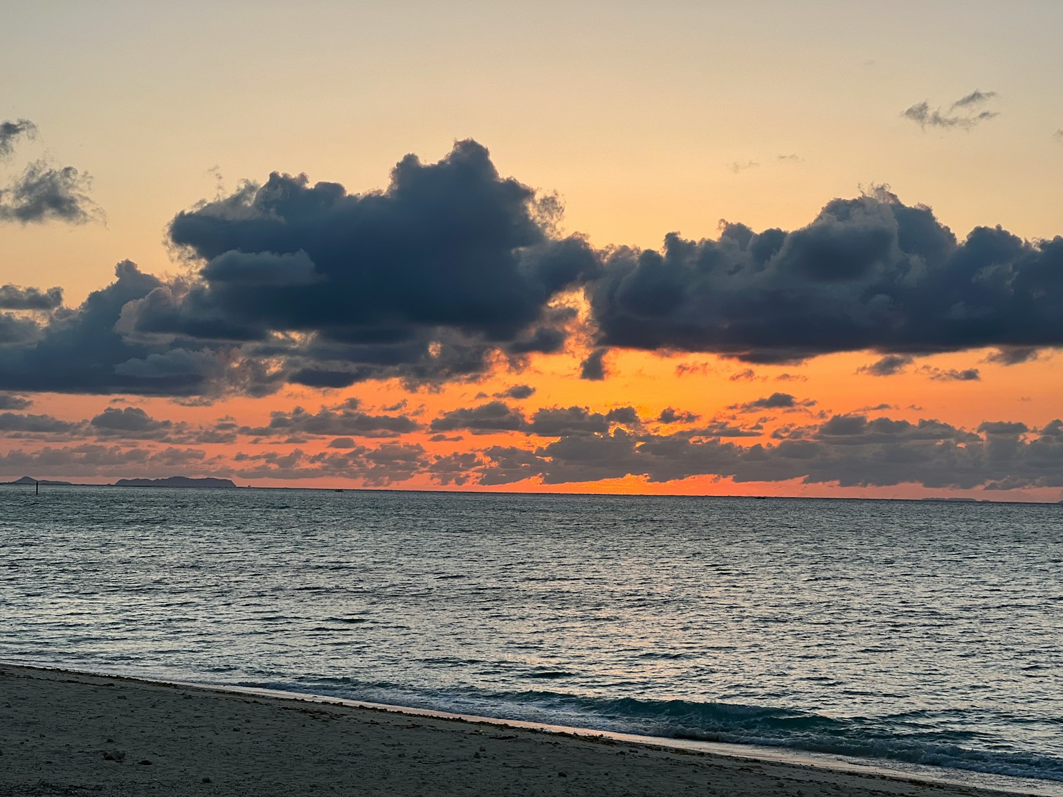 日落时宁静的海滩场景，伴有云朵和海浪