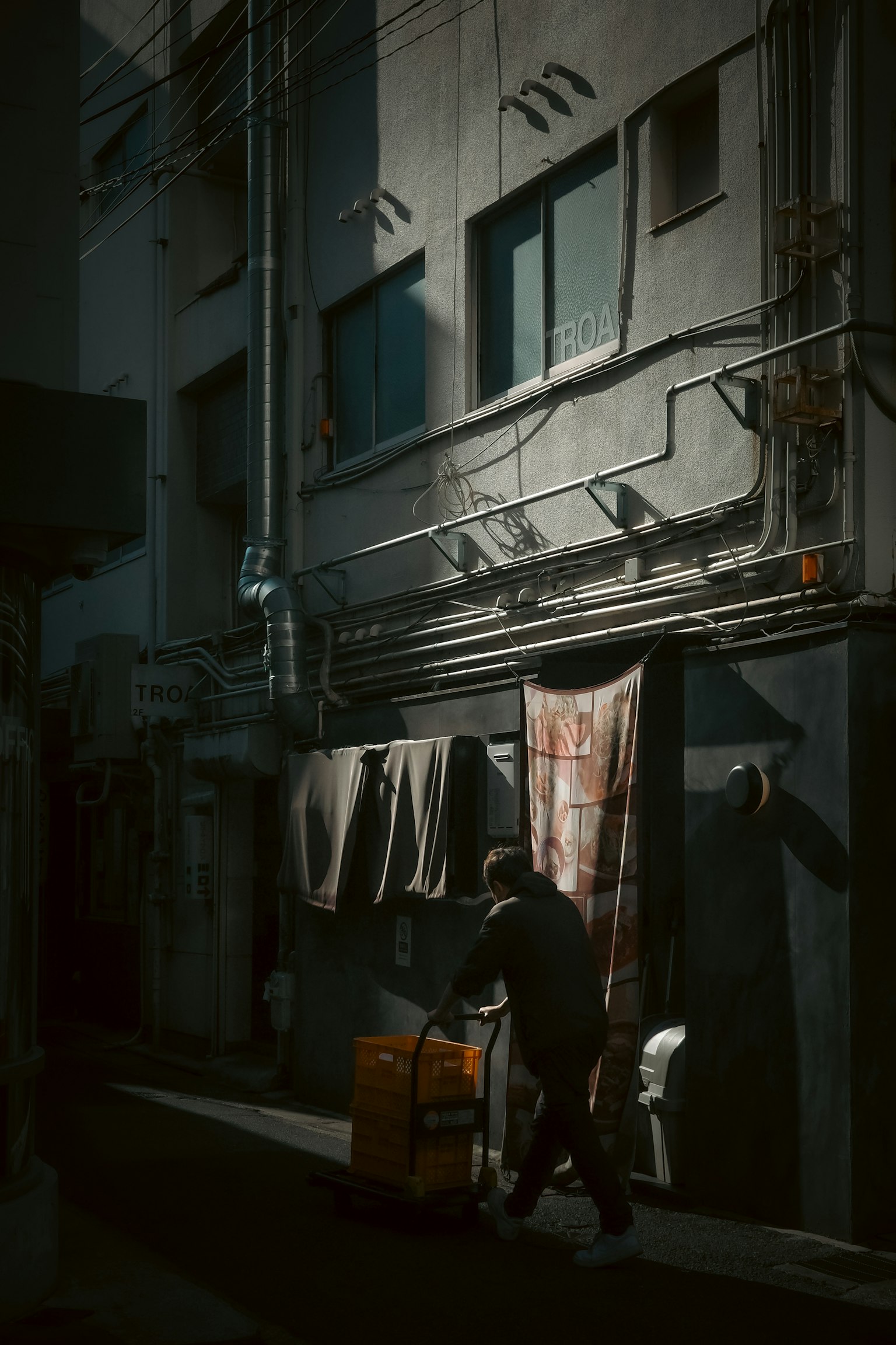 A person pushing a cart in a dark alley with laundry hanging