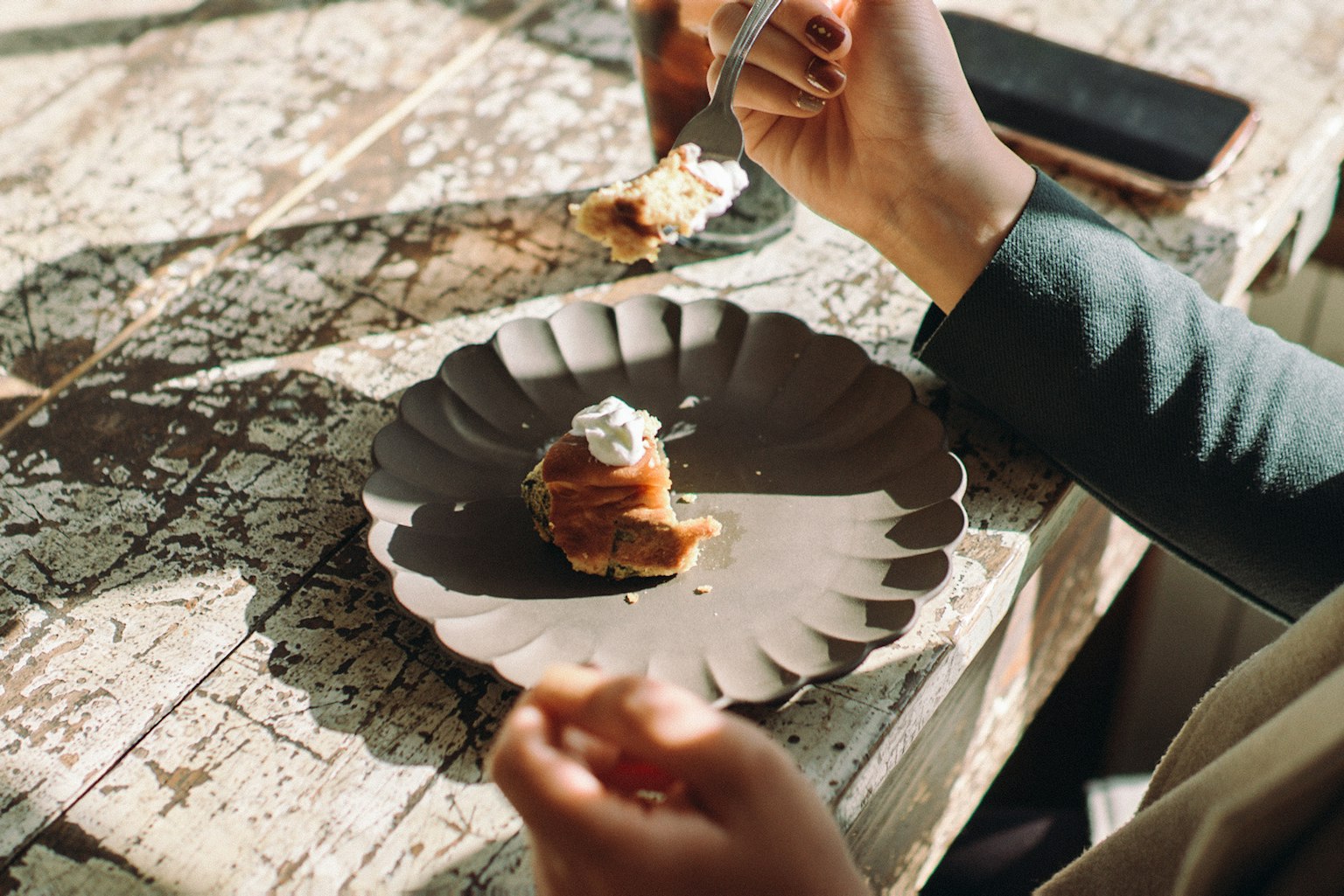 Personne tenant une cuillère dégustant un dessert sur une assiette noire