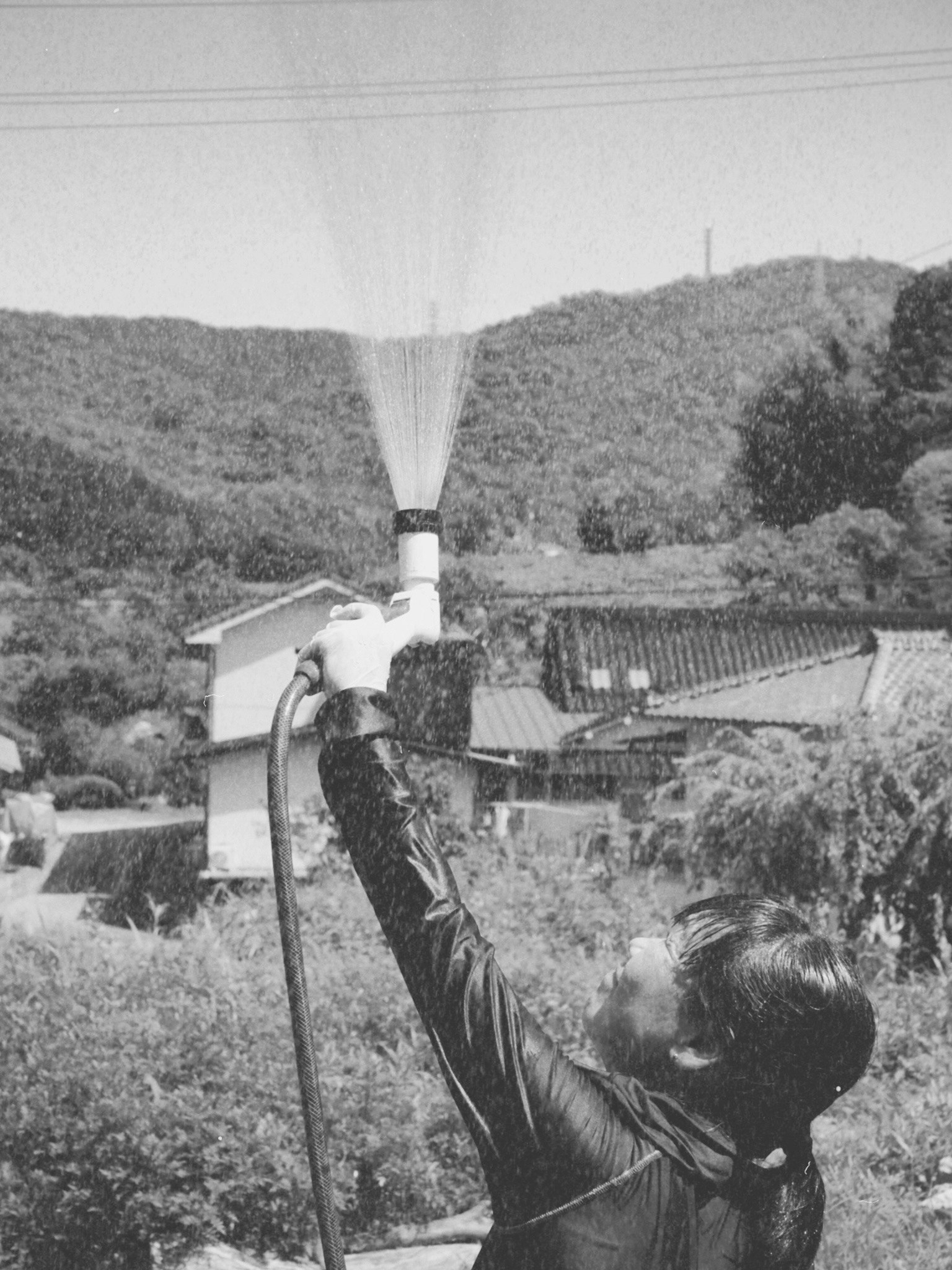 黒白の写真でホースを持ち空に向かって水を噴射している男性