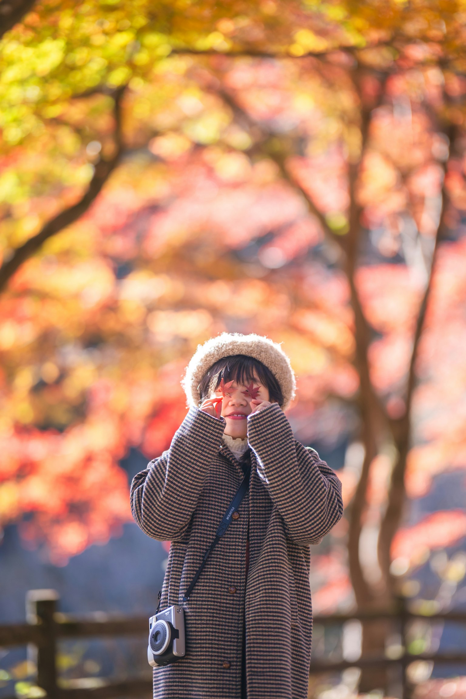 Người phụ nữ tạo dáng giữa những tán lá mùa thu mặc áo khoác ấm và mũ cầm máy ảnh