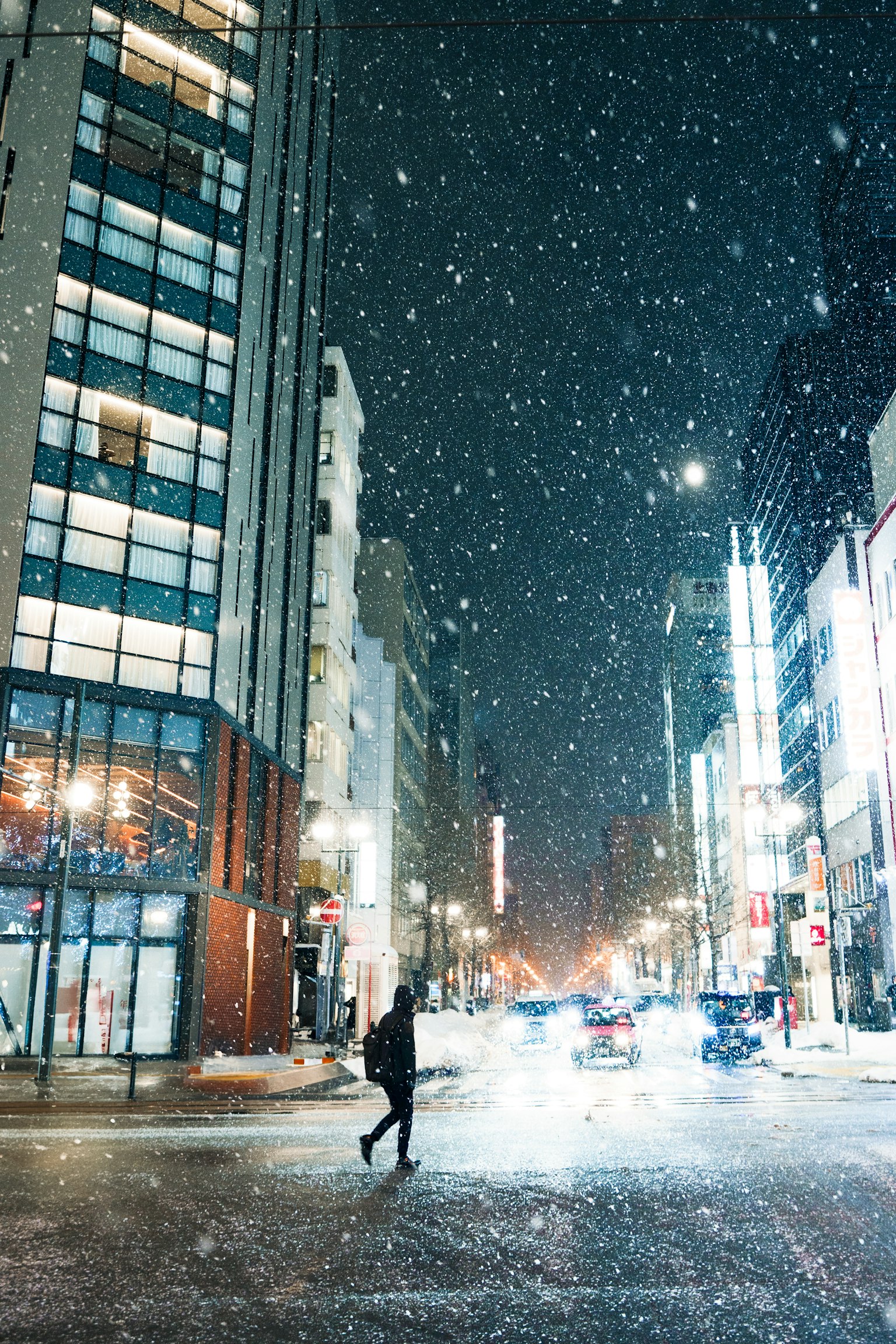 夜間雪天街道上行人的景象，背景有建築物