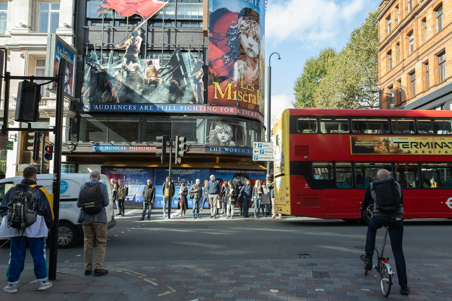 Cảnh đường phố nhộn nhịp ở London với quảng cáo nhạc kịch trên tòa nhà và xe buýt đỏ