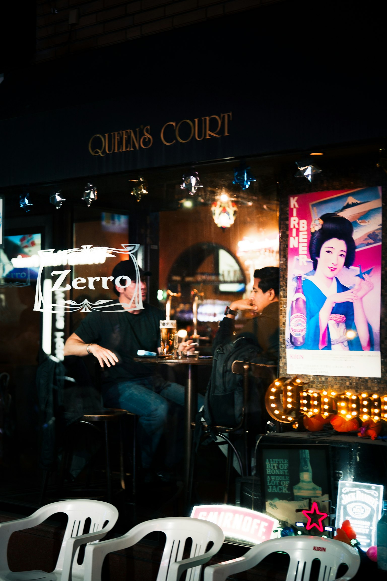 Due uomini seduti all'interno di un bar con insegne colorate sullo sfondo