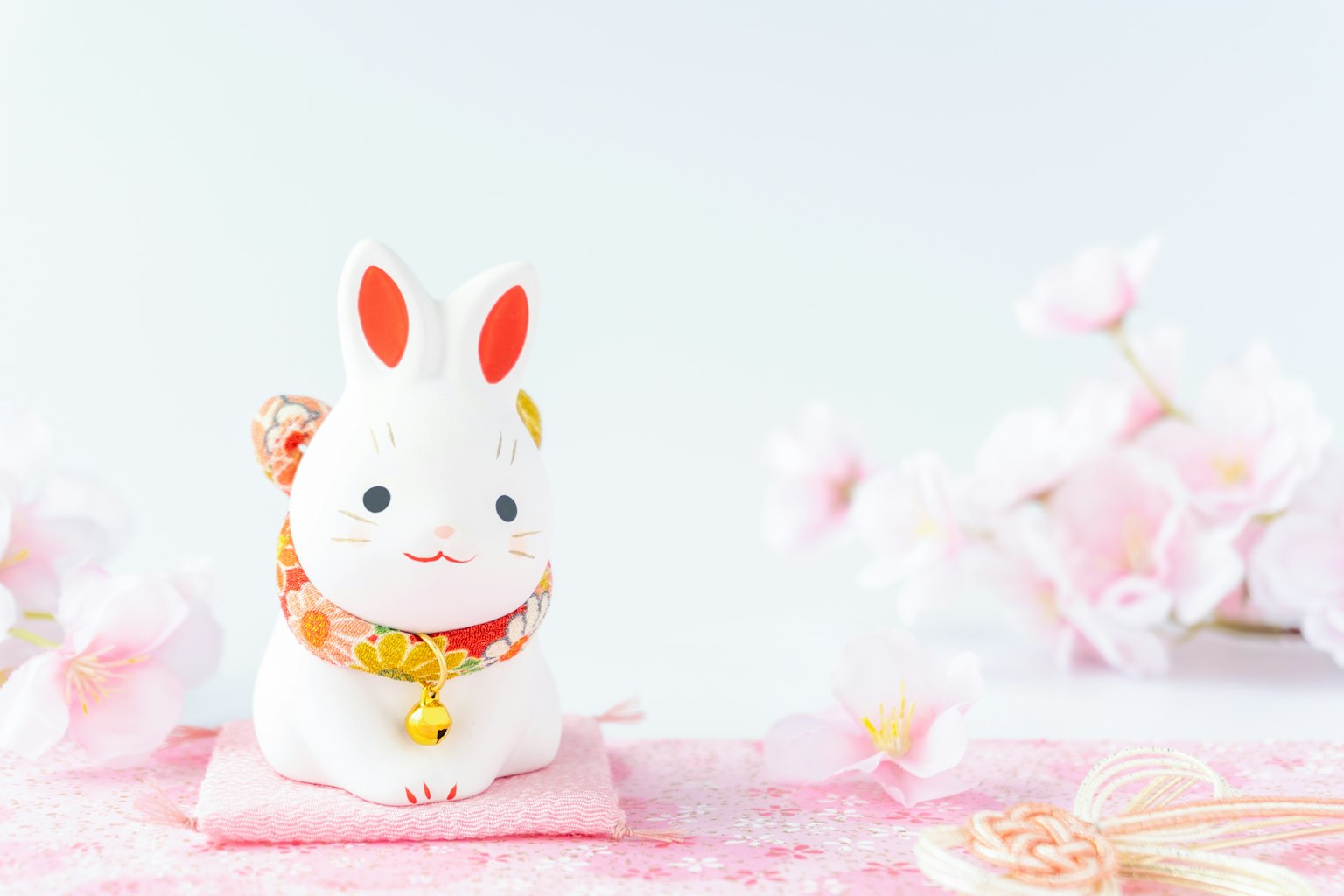 Một bức tượng thỏ trắng ngồi trên thảm hồng xung quanh là cánh hoa anh đào
