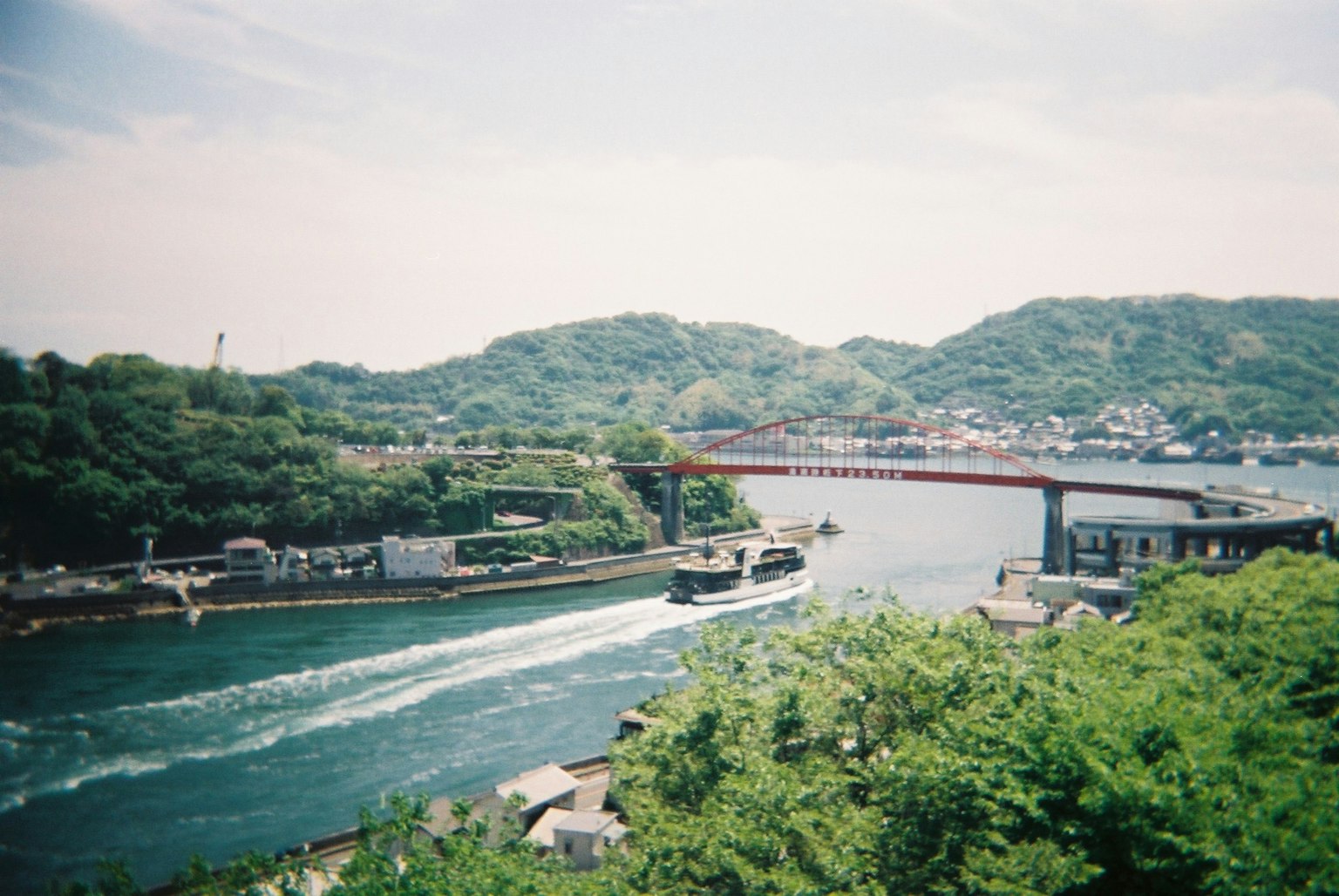 Vista panoramica di un fiume con colline verdi e un ponte rosso Una barca che naviga sull'acqua
