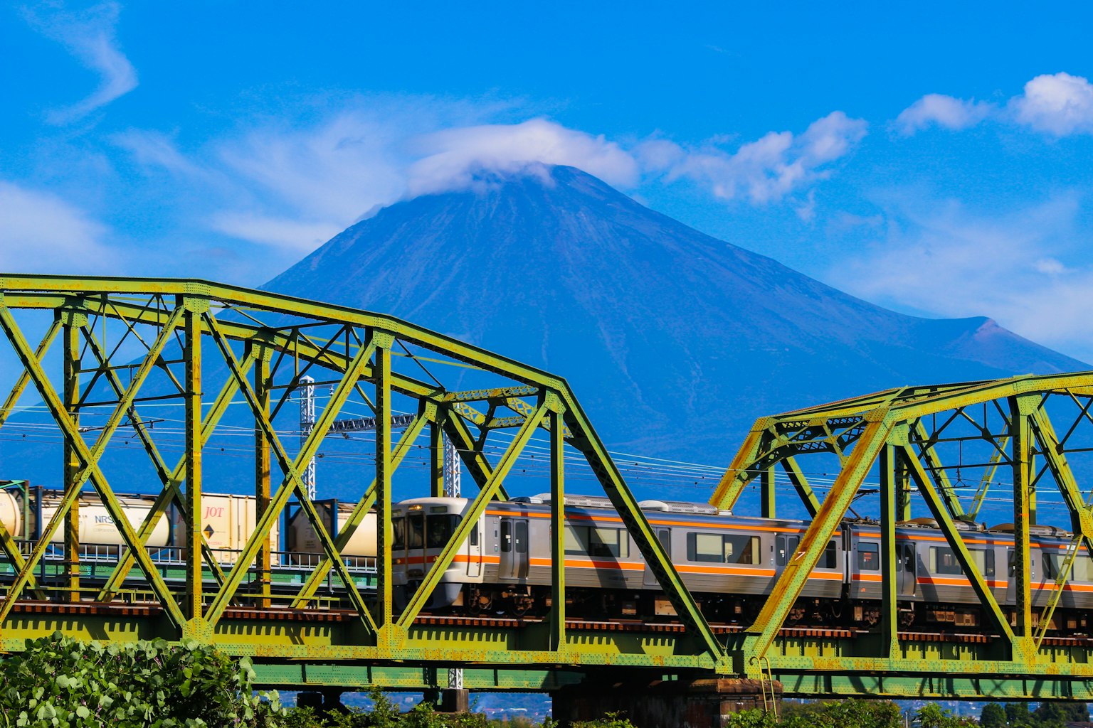 Train crossing a green bridge with Mount Fuji in the background
