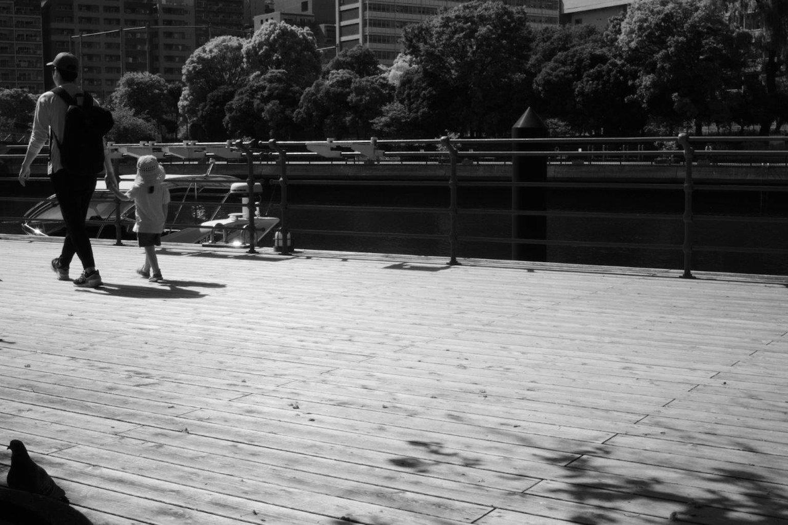 Silhouette of an adult and child walking on a wooden deck black and white scene with greenery in the background
