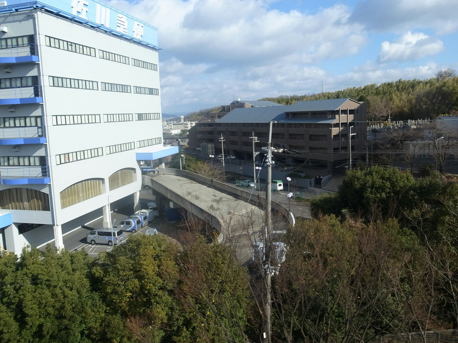 Vue d'un bâtiment au toit bleu entouré de verdure et d'infrastructure urbaine