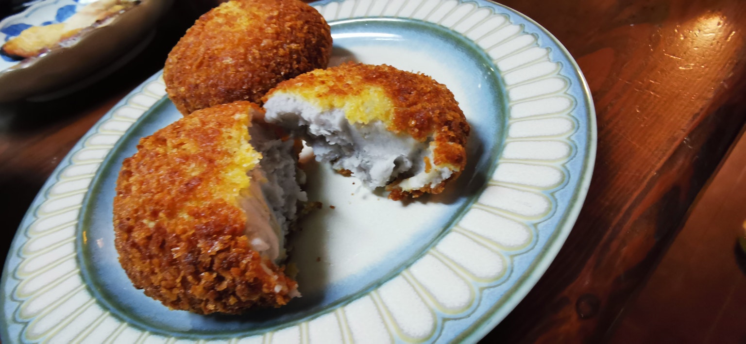 A plate of fried croquettes with a cut piece showing the filling