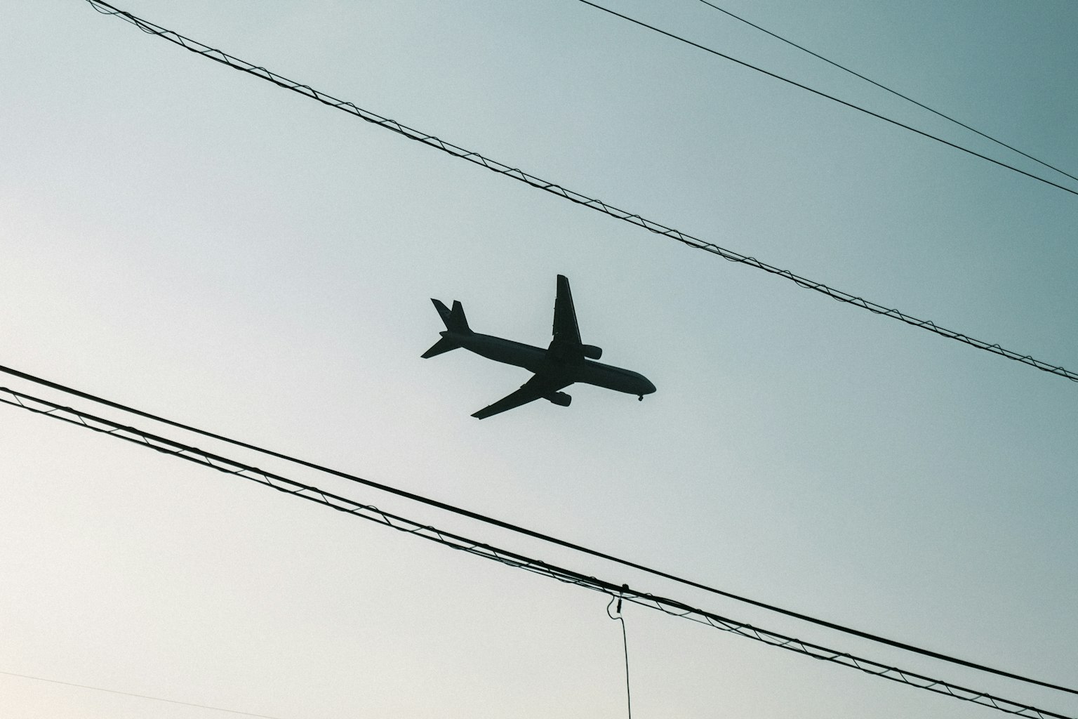 Silhouette eines Flugzeugs, das gegen einen hellen Himmel mit Stromleitungen fliegt