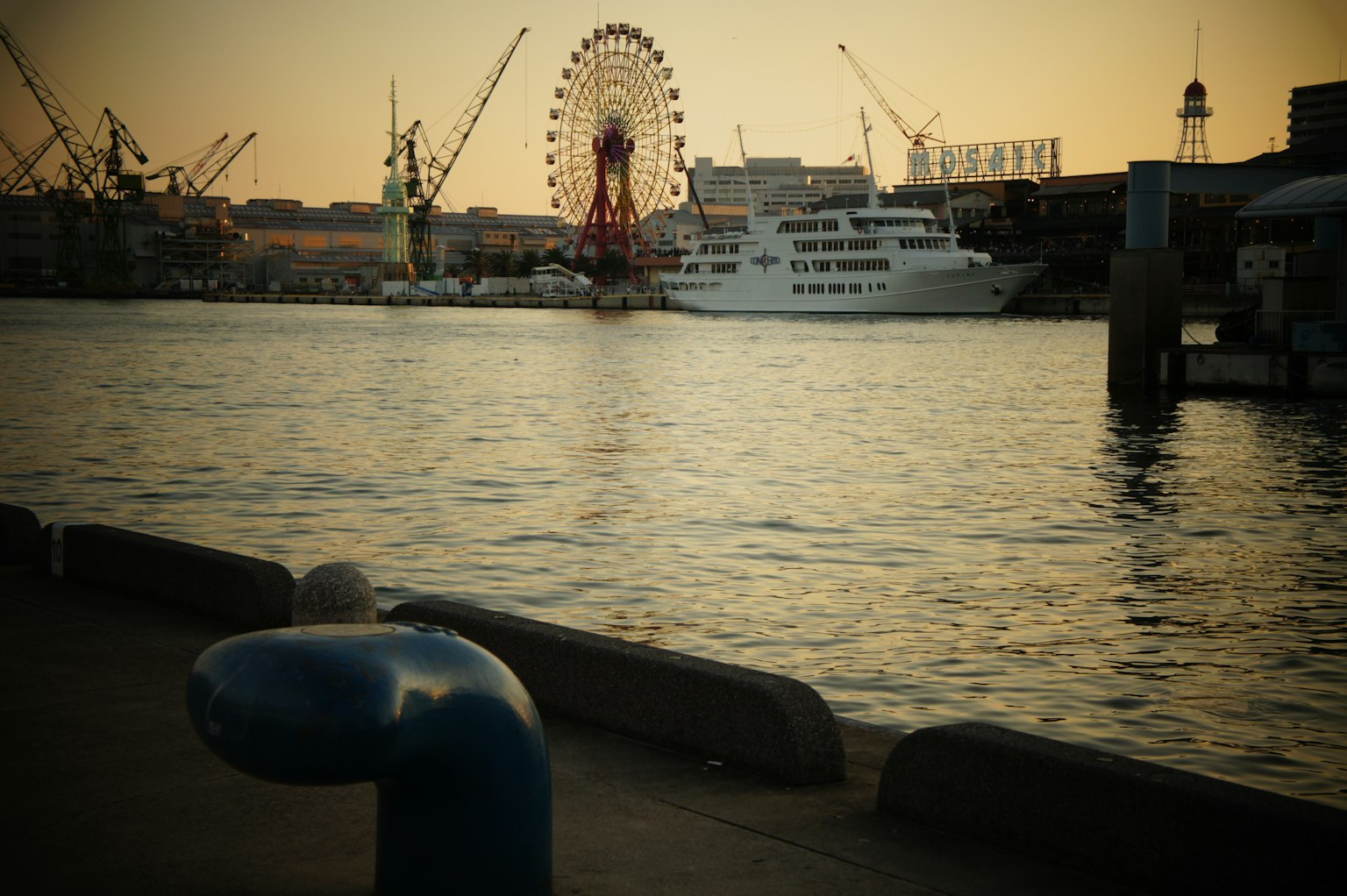 Harbor scene at sunset featuring a ship and a Ferris wheel