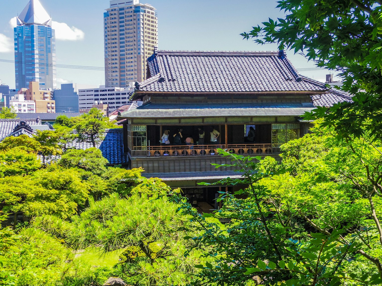 傳統日本房屋被綠樹環繞，背景是現代摩天大樓
