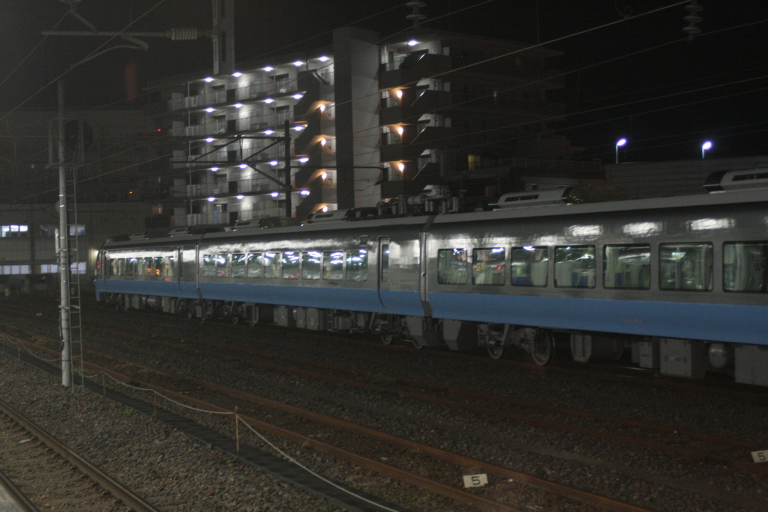 Kereta biru di malam hari dengan bangunan yang diterangi di latar belakang