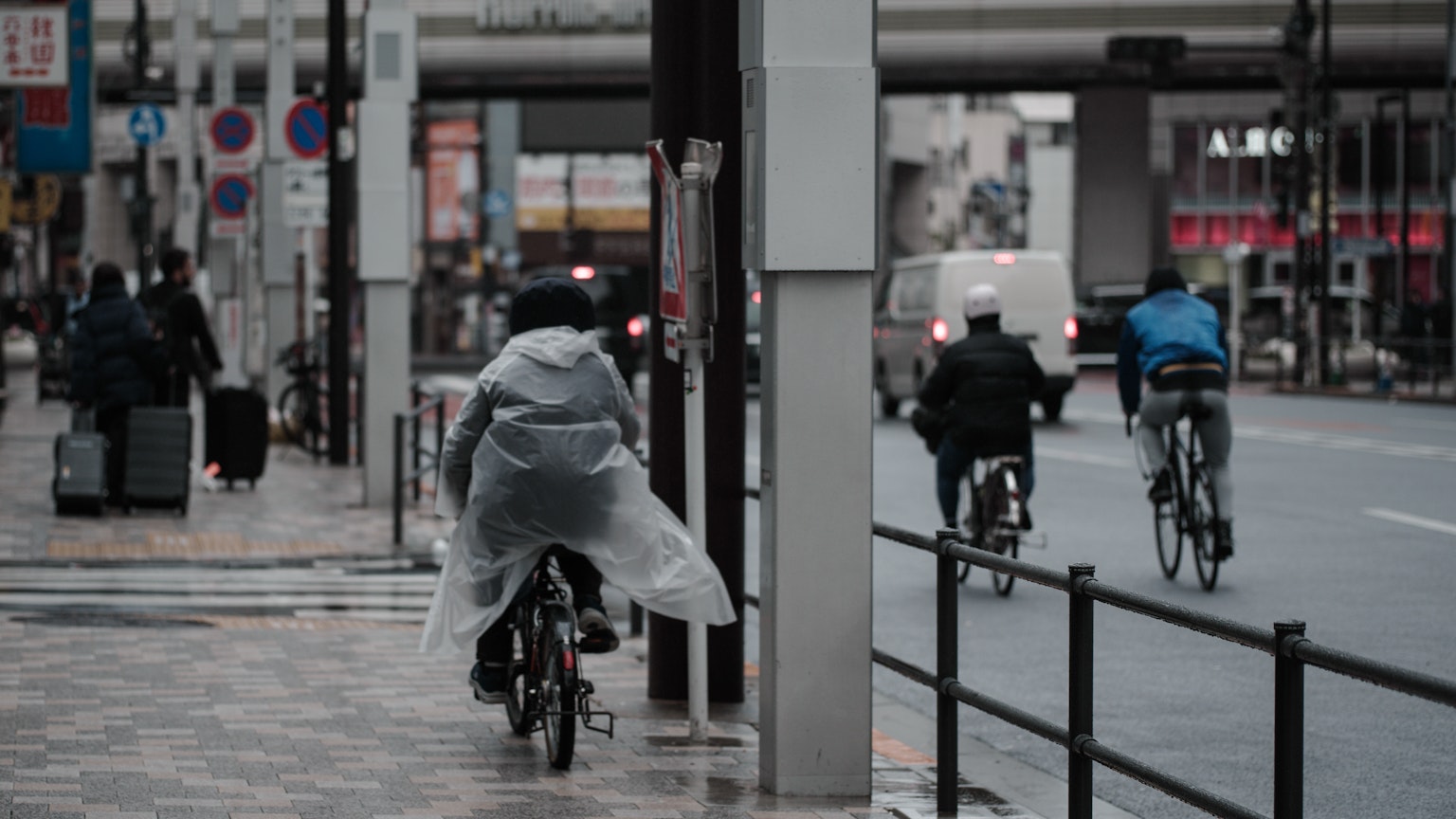 Persone in bicicletta sotto la pioggia con paesaggio urbano