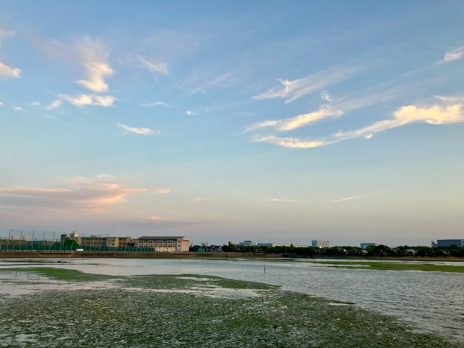 Landscape featuring a blue sky with clouds over a flooded field and buildings