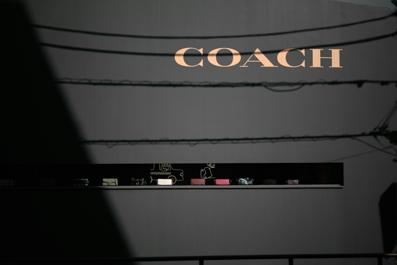 Vue extérieure d'un magasin avec une enseigne Coach et des ombres