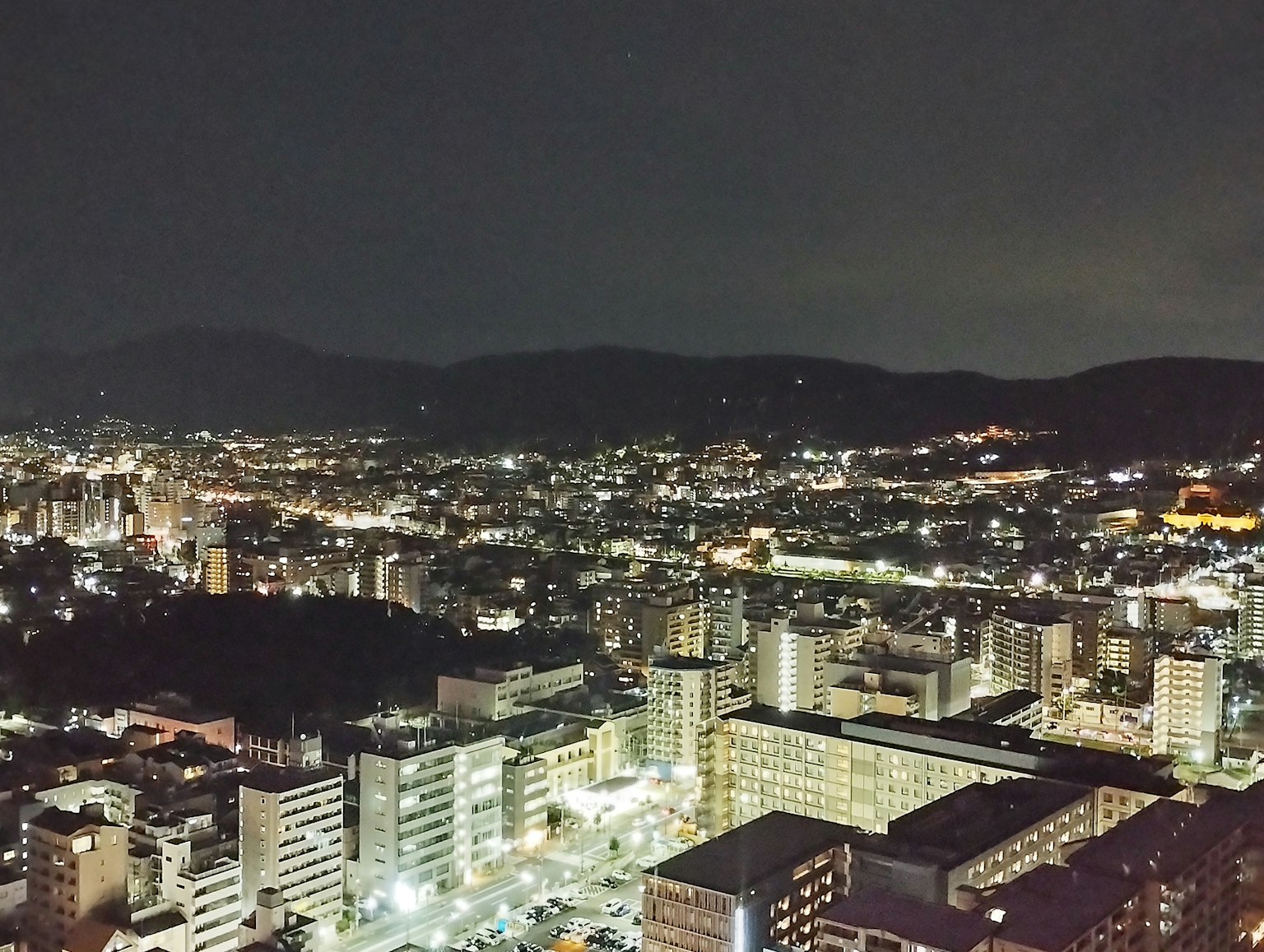 Panoramic night cityscape with illuminated buildings and mountains