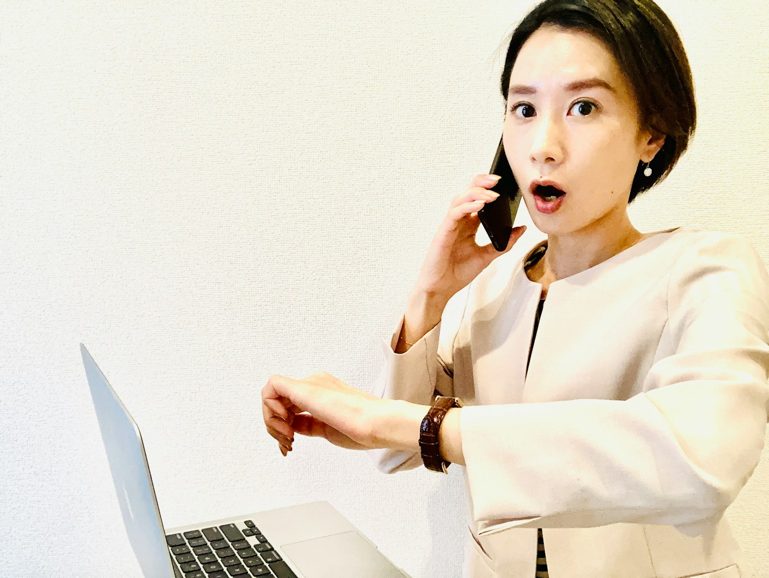 Seorang wanita terkejut berbicara di telepon sambil melihat laptopnya