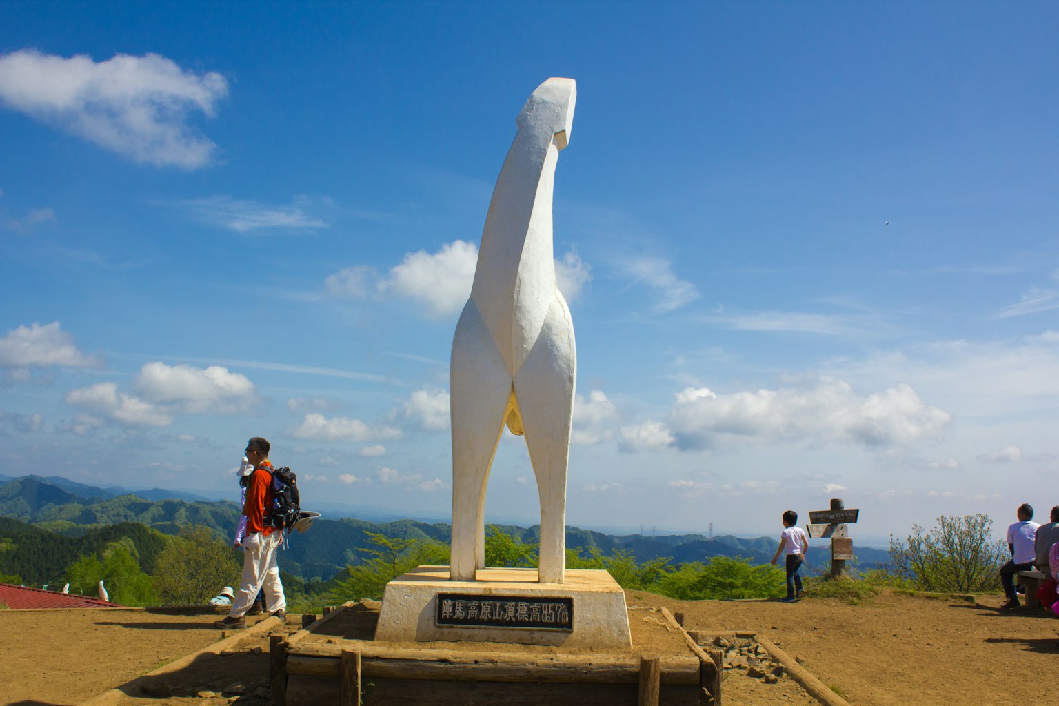 A white dog statue stands at the mountain peak with people gathered around