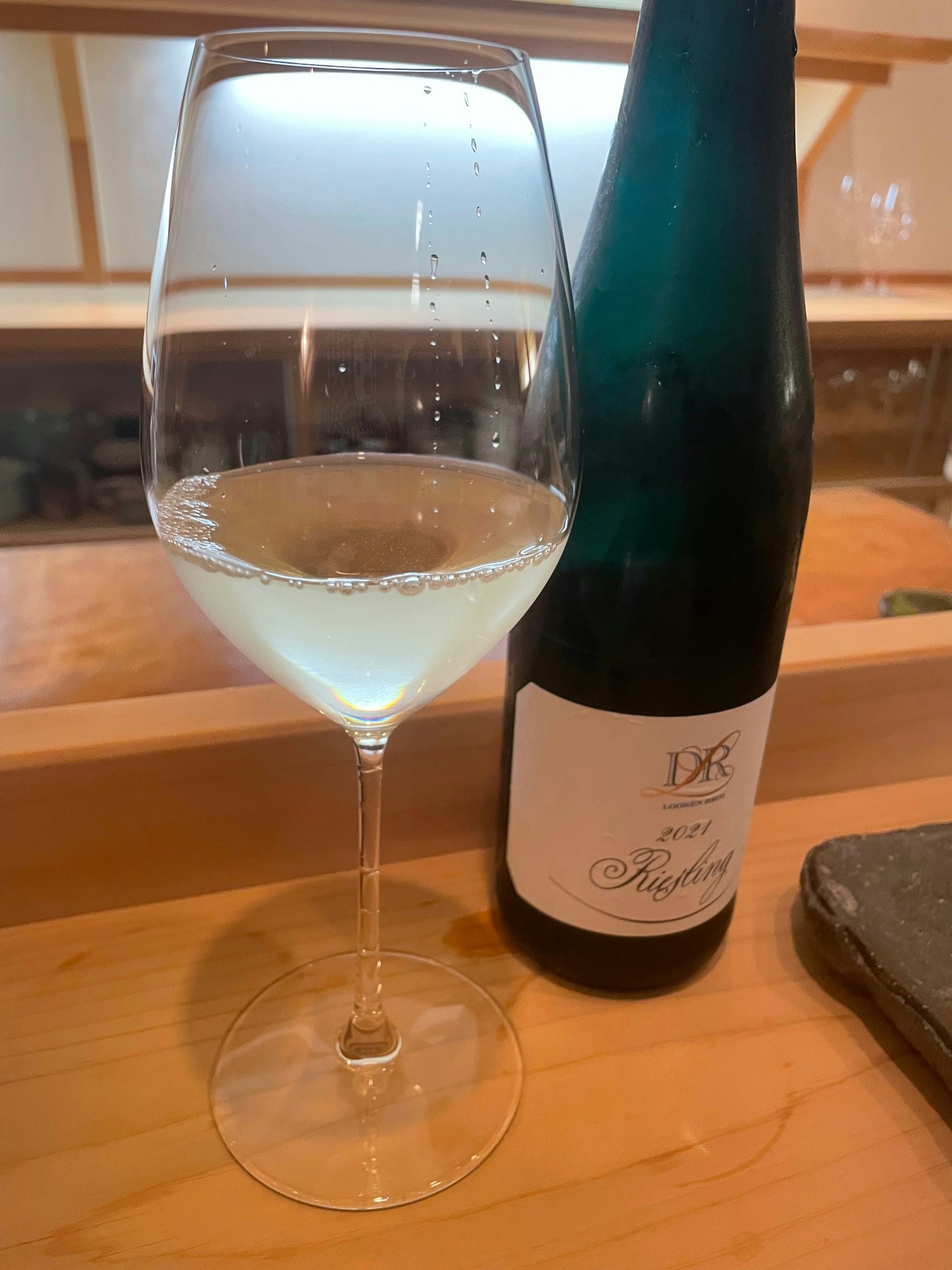 Un hermoso vaso de vino blanco junto a una botella verde