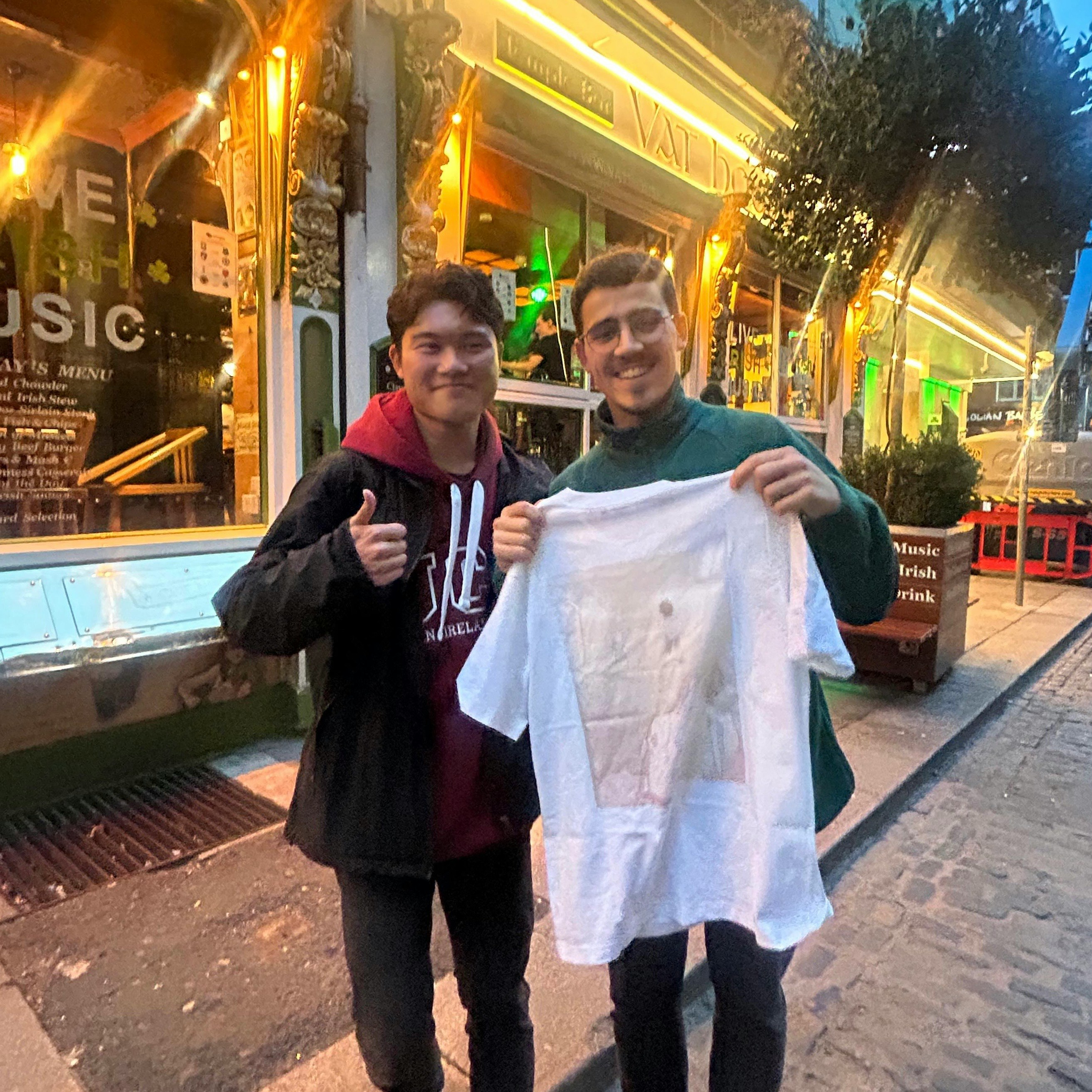 夜の屋外で屋台通りを歩く2人がTシャツを掲げる