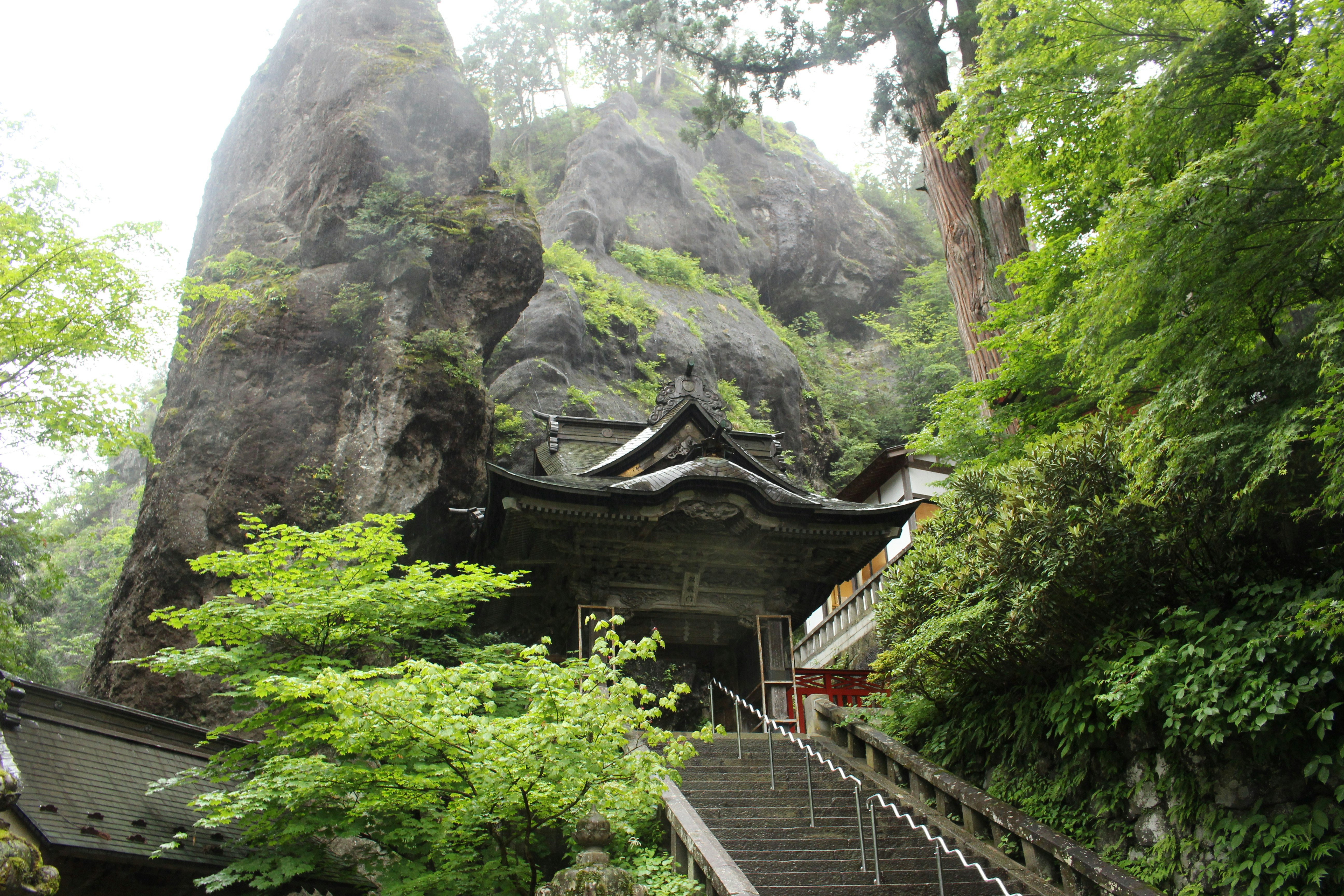 巨岩の岩壁に寄り添う神社の社殿と石段