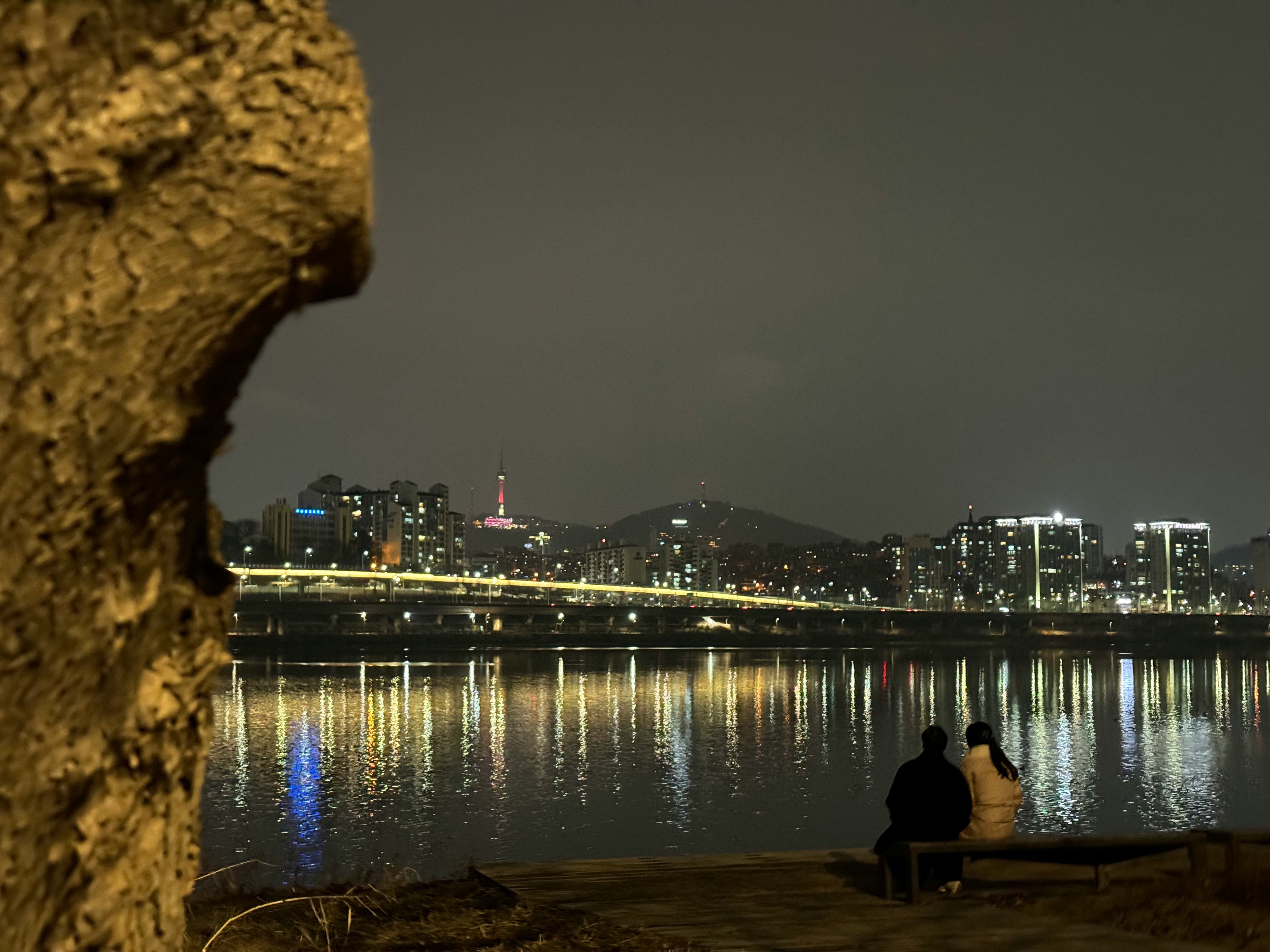 川沿いのベンチで夜景を見つめるカップル