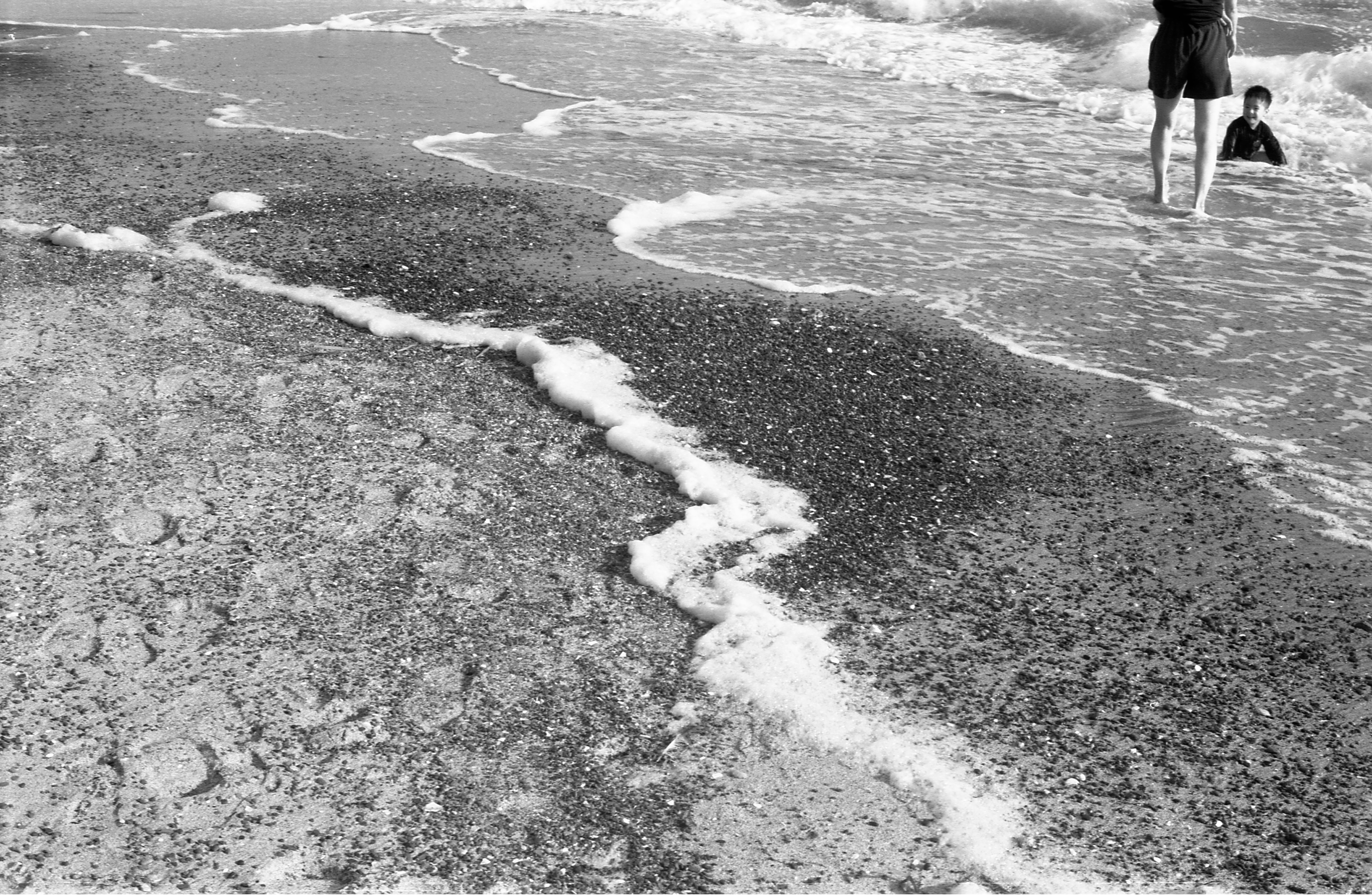 orang berjalan di sepanjang pantai berpasir dengan ombak berbusa