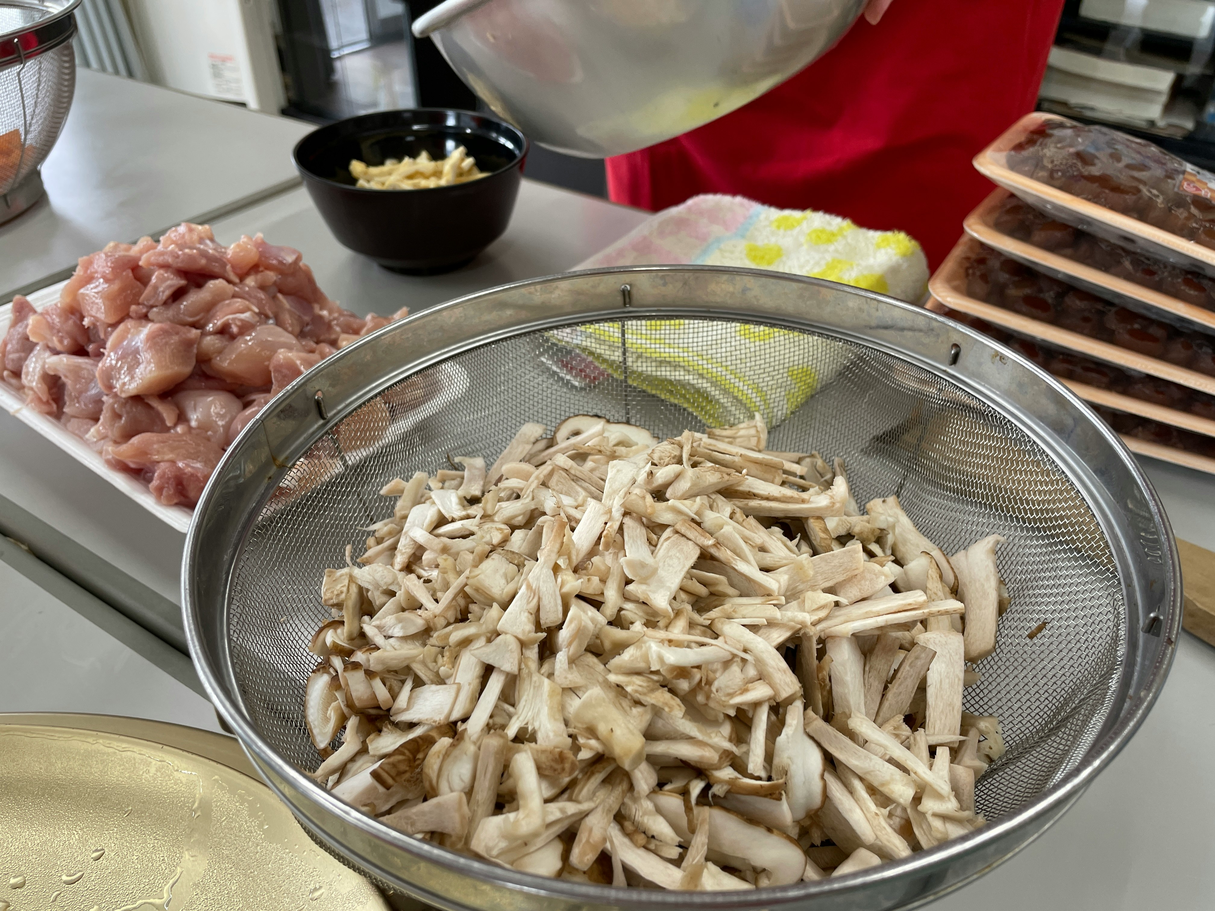 まな板の上で調理用の鶏肉ときのこをザルで水切りしているキッチン風景