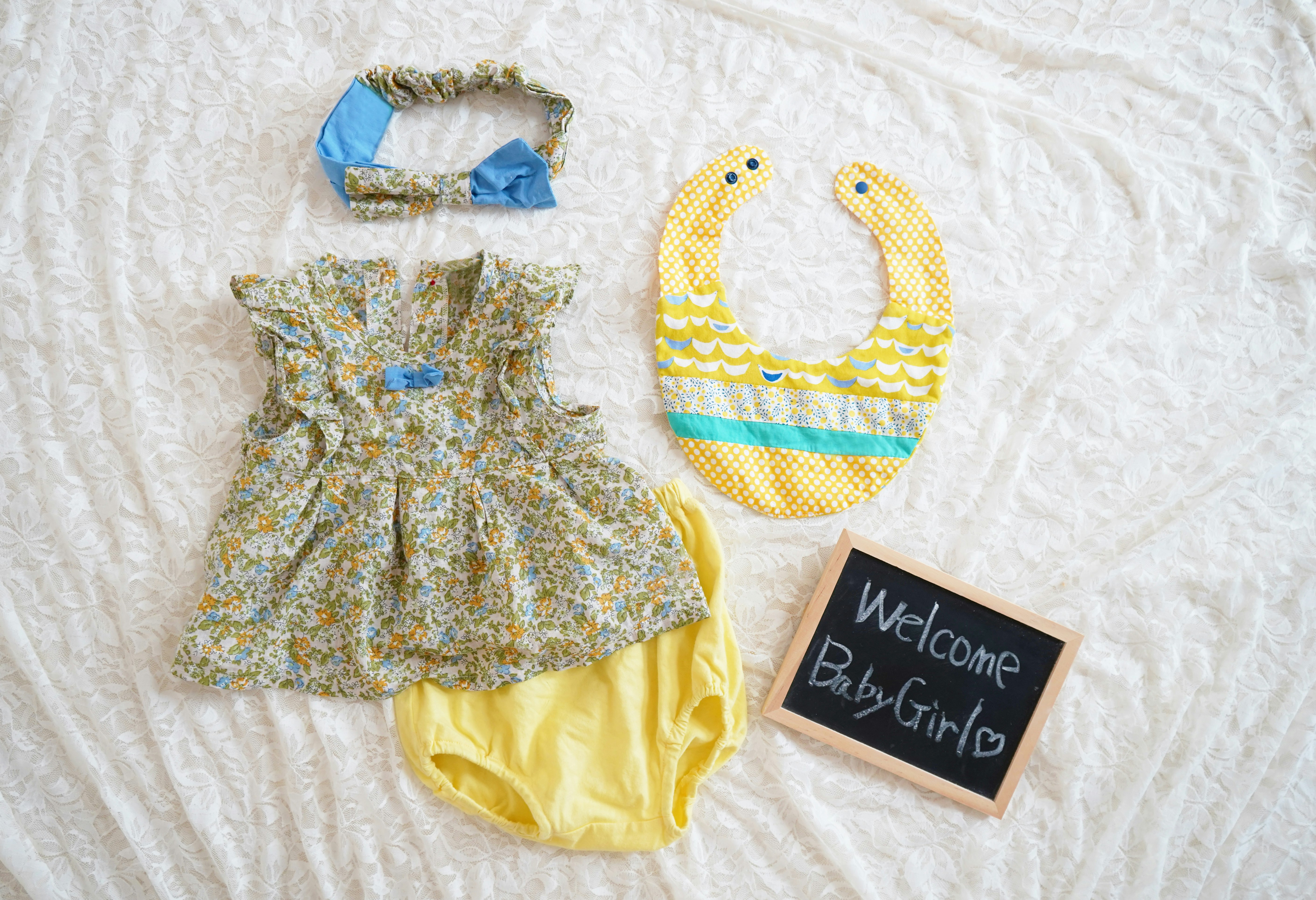 ropa de bebé y babero con un letrero “Welcome Baby Girl”