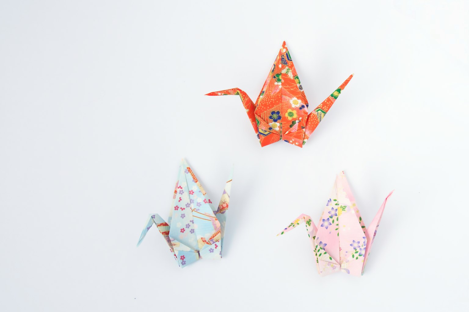 Drei farbenfrohe Origami-Kraniche auf einem schlichten Hintergrund angeordnet