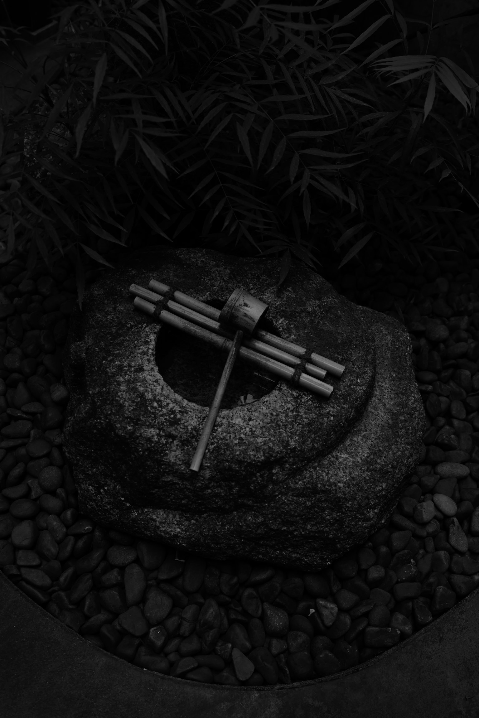 Immagine in bianco e nero che presenta una scultura di pietra e una struttura in bambù in un giardino