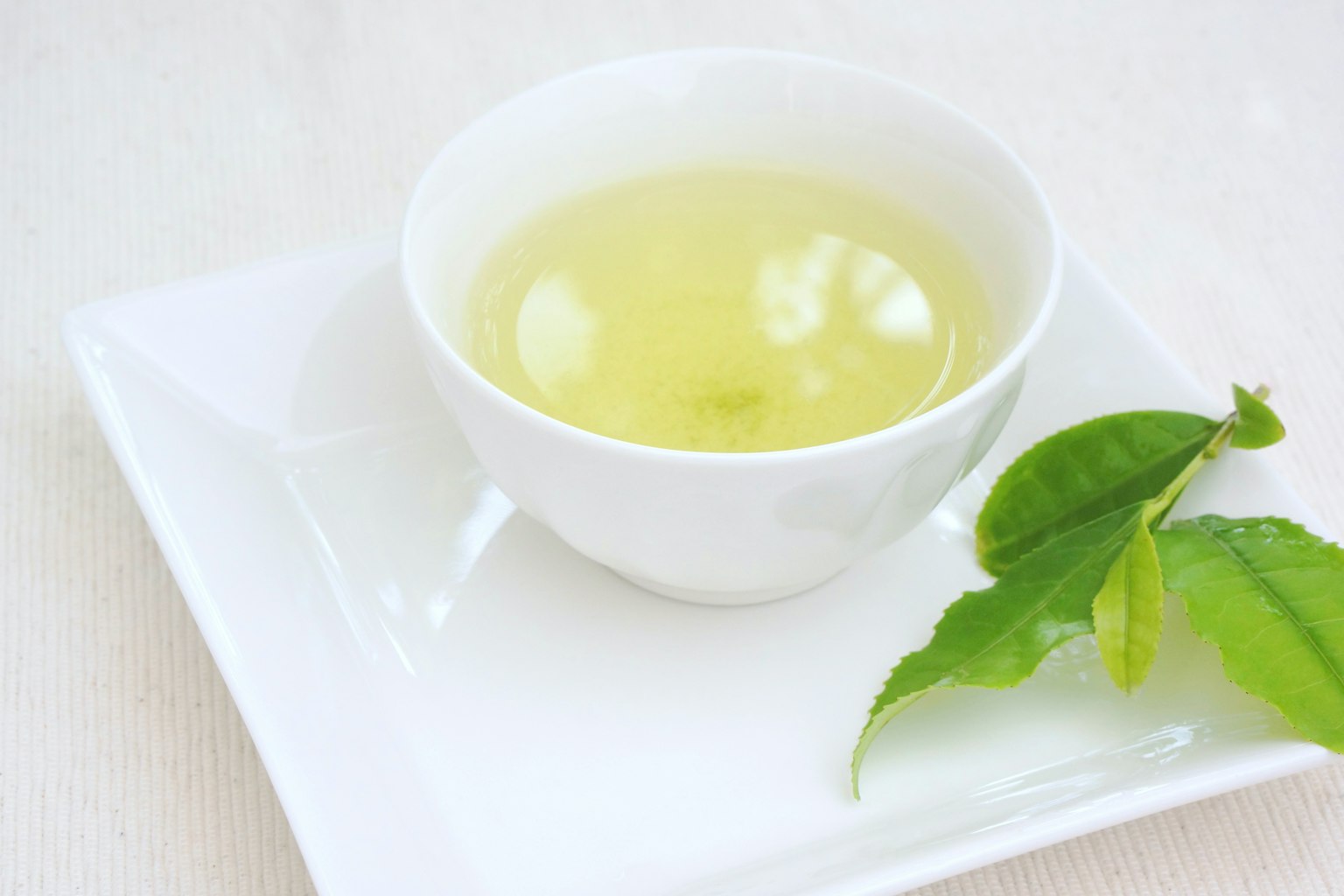 白色杯子裡的綠茶和旁邊的綠茶葉