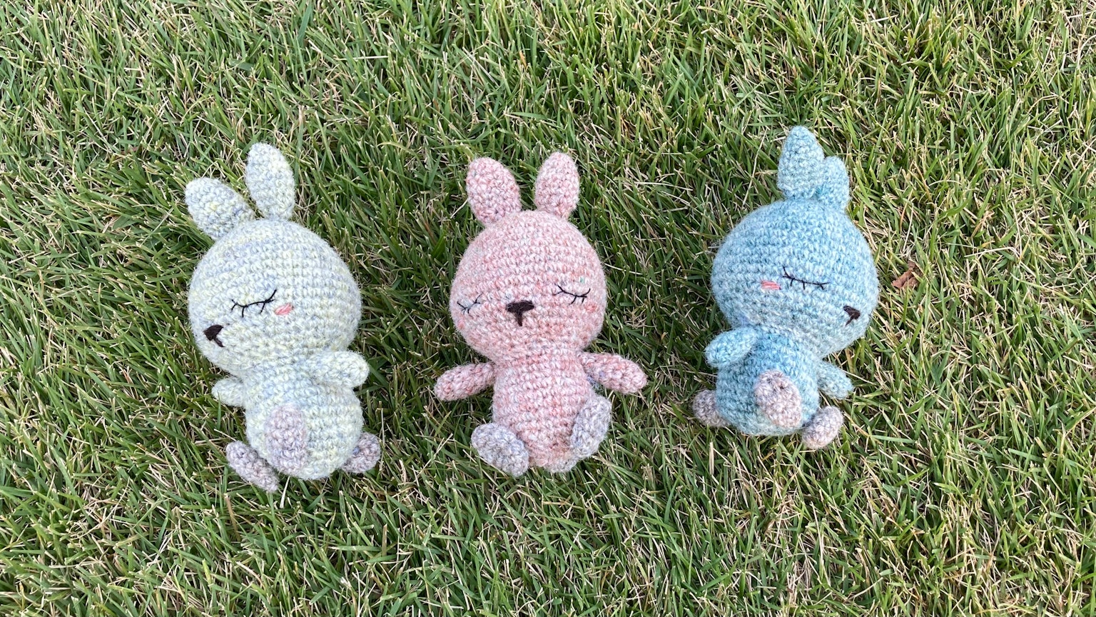 Tres juguetes de peluche de conejito coloridos dispuestos sobre hierba verde