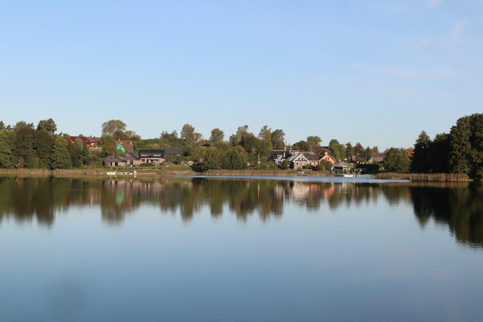 Danau tenang yang memantulkan rumah dan pohon di latar belakang