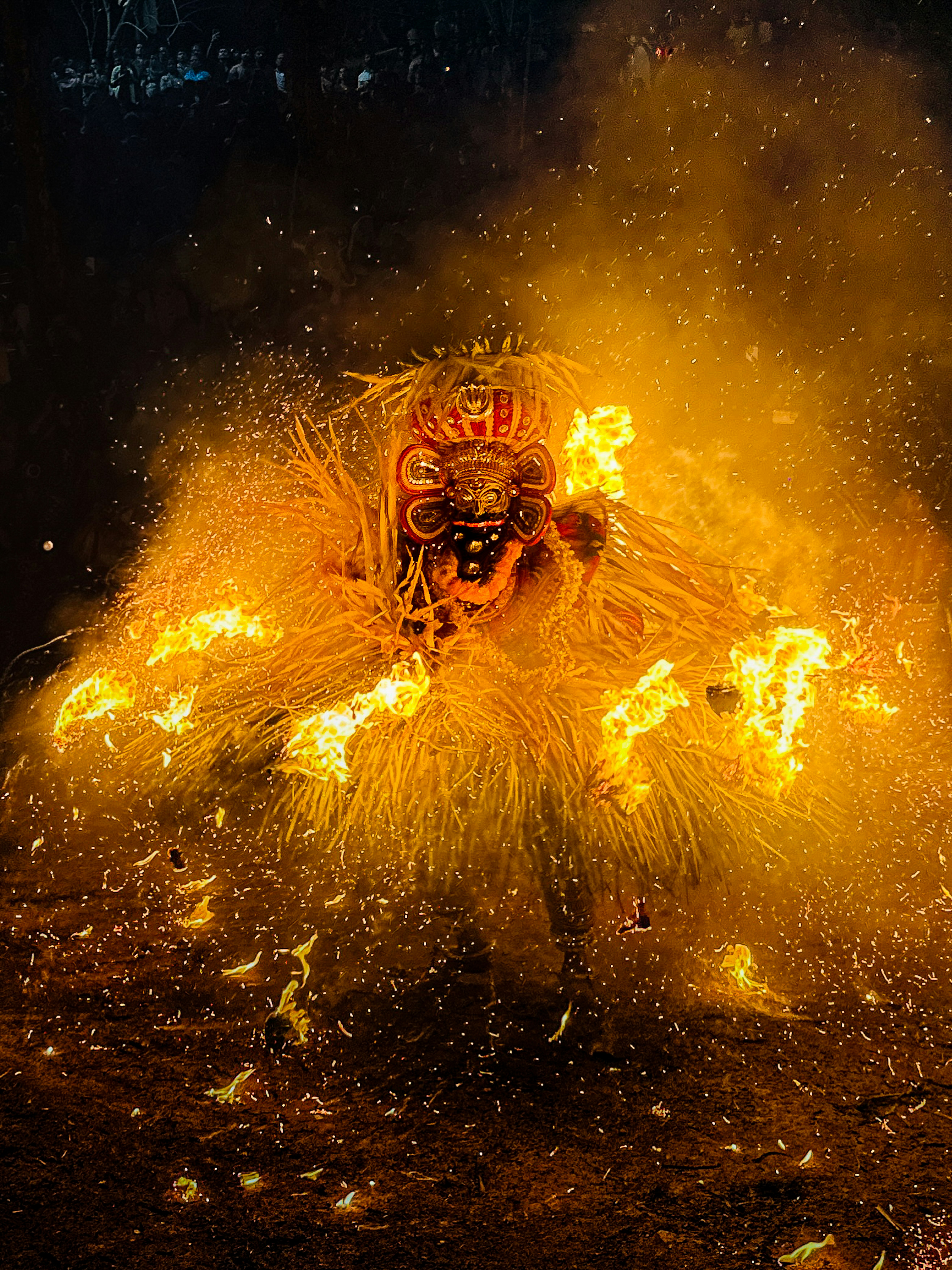 Theyyam ritual moment with a masked performer amid flames and sparks