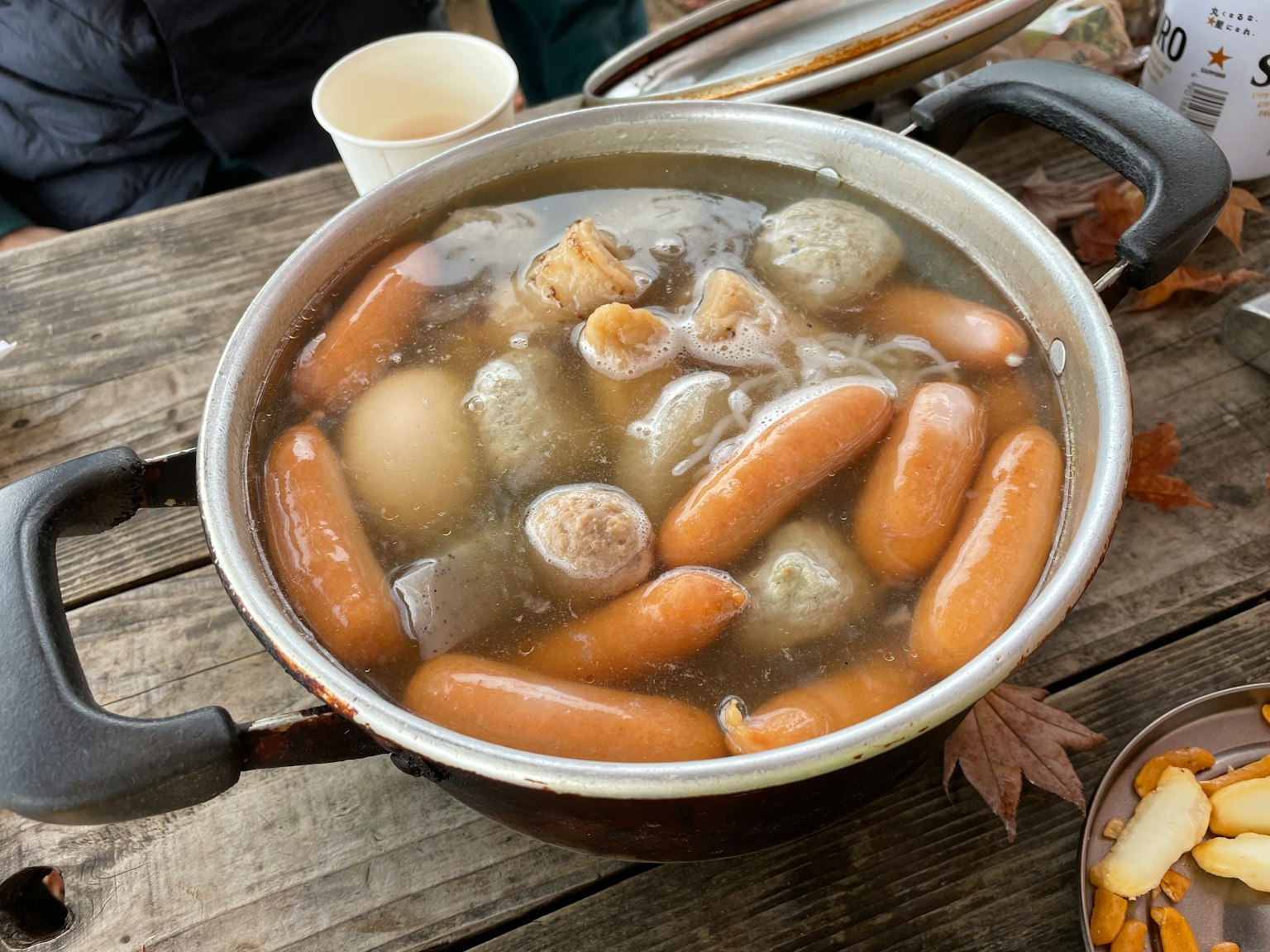 A pot filled with sausages, dumplings, and eggs in broth