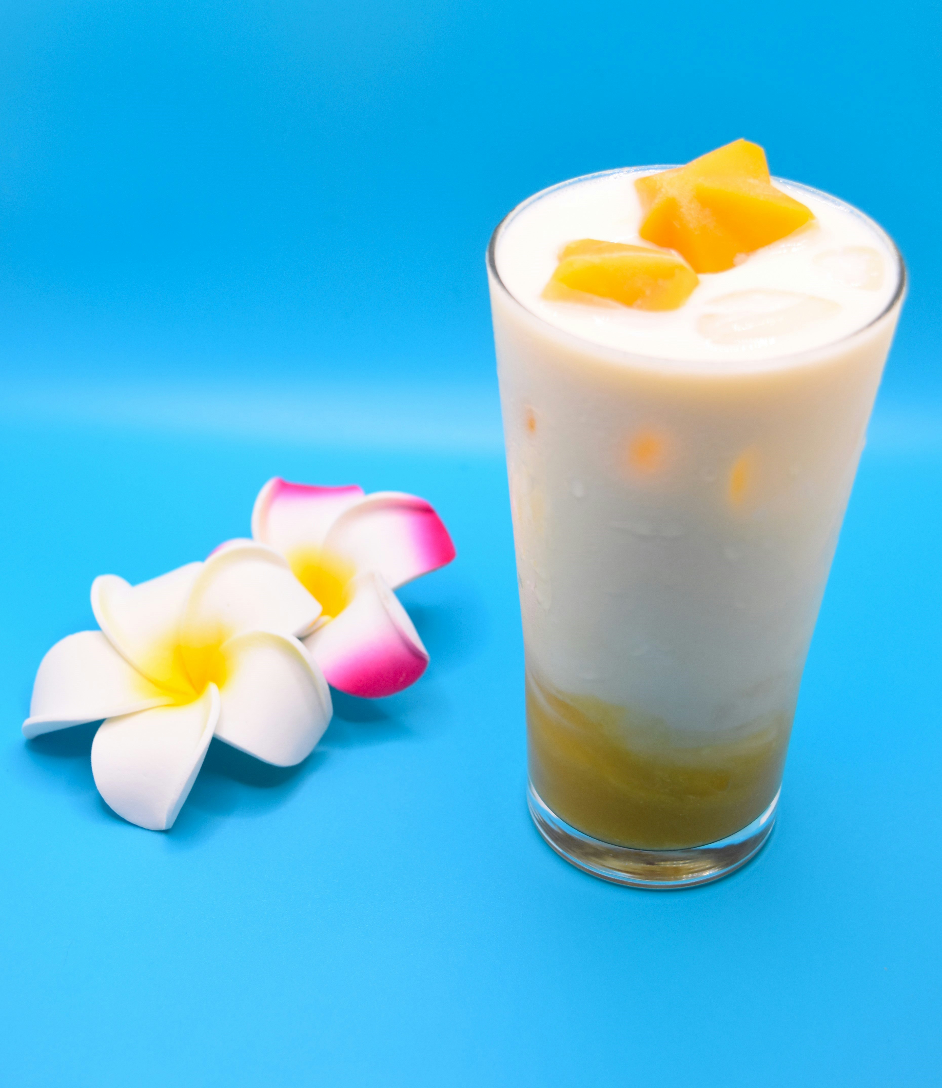 Đồ uống sữa chua xoài kèm trang trí hoa trên nền xanh